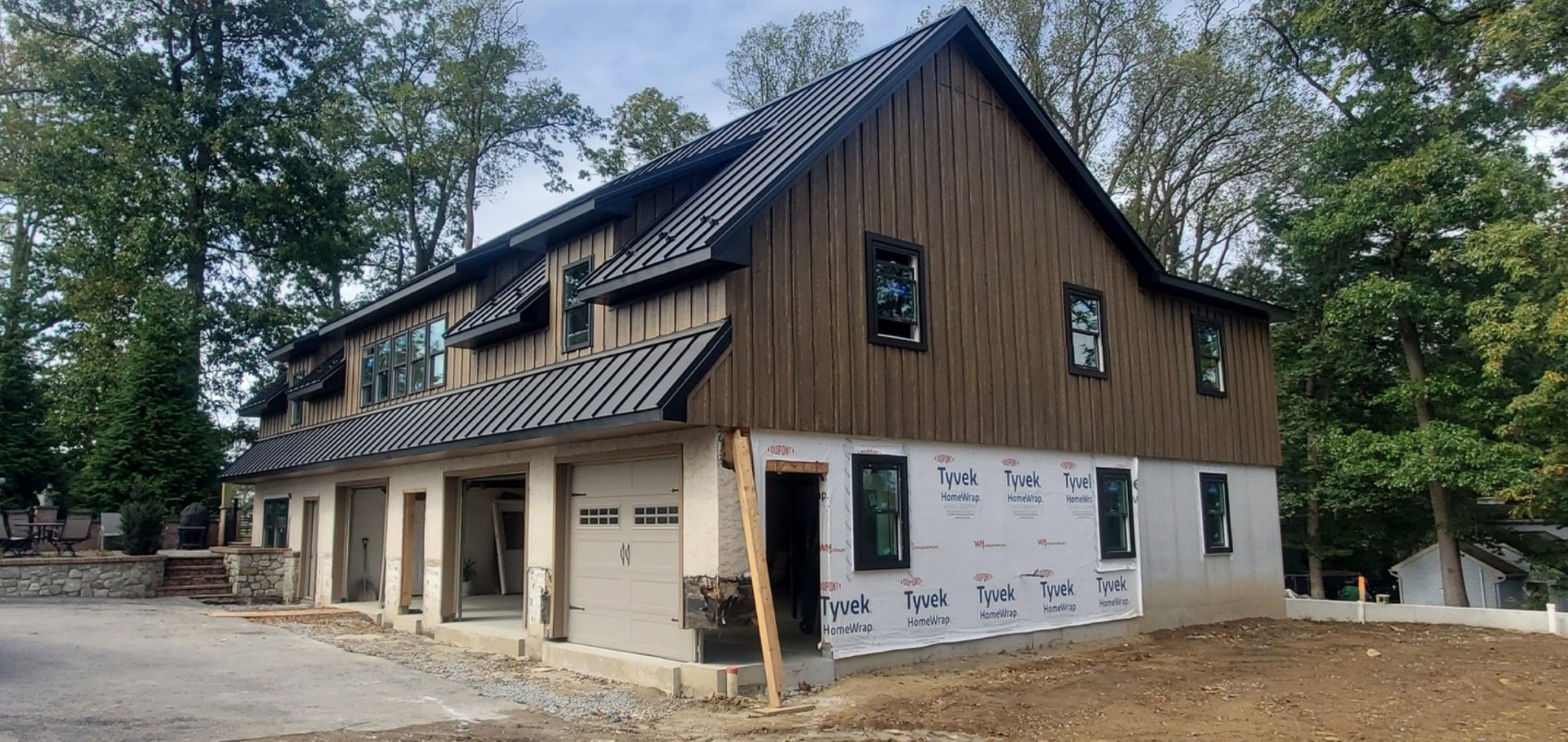 Two-story house under construction with brown siding, black roof, and windows.