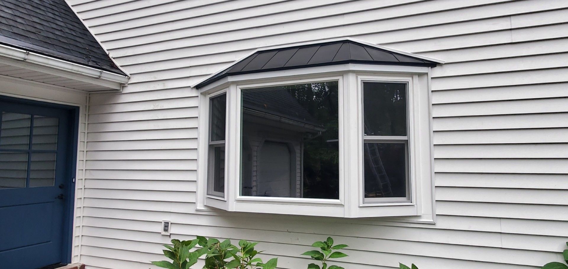 White house with a dark blue door and a bay window.