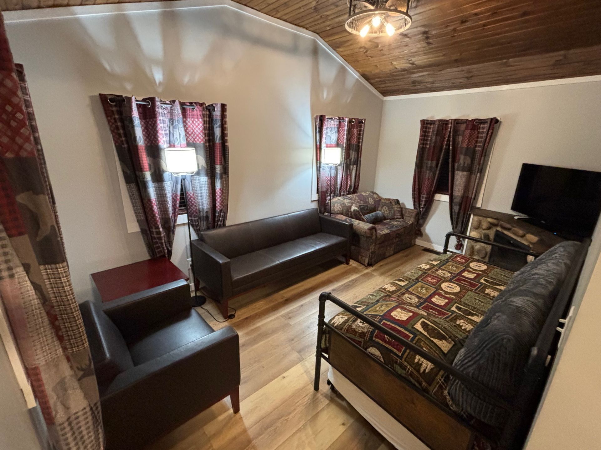 Living room with furniture, including a couch, chairs, and a daybed, with patterned curtains and a TV.