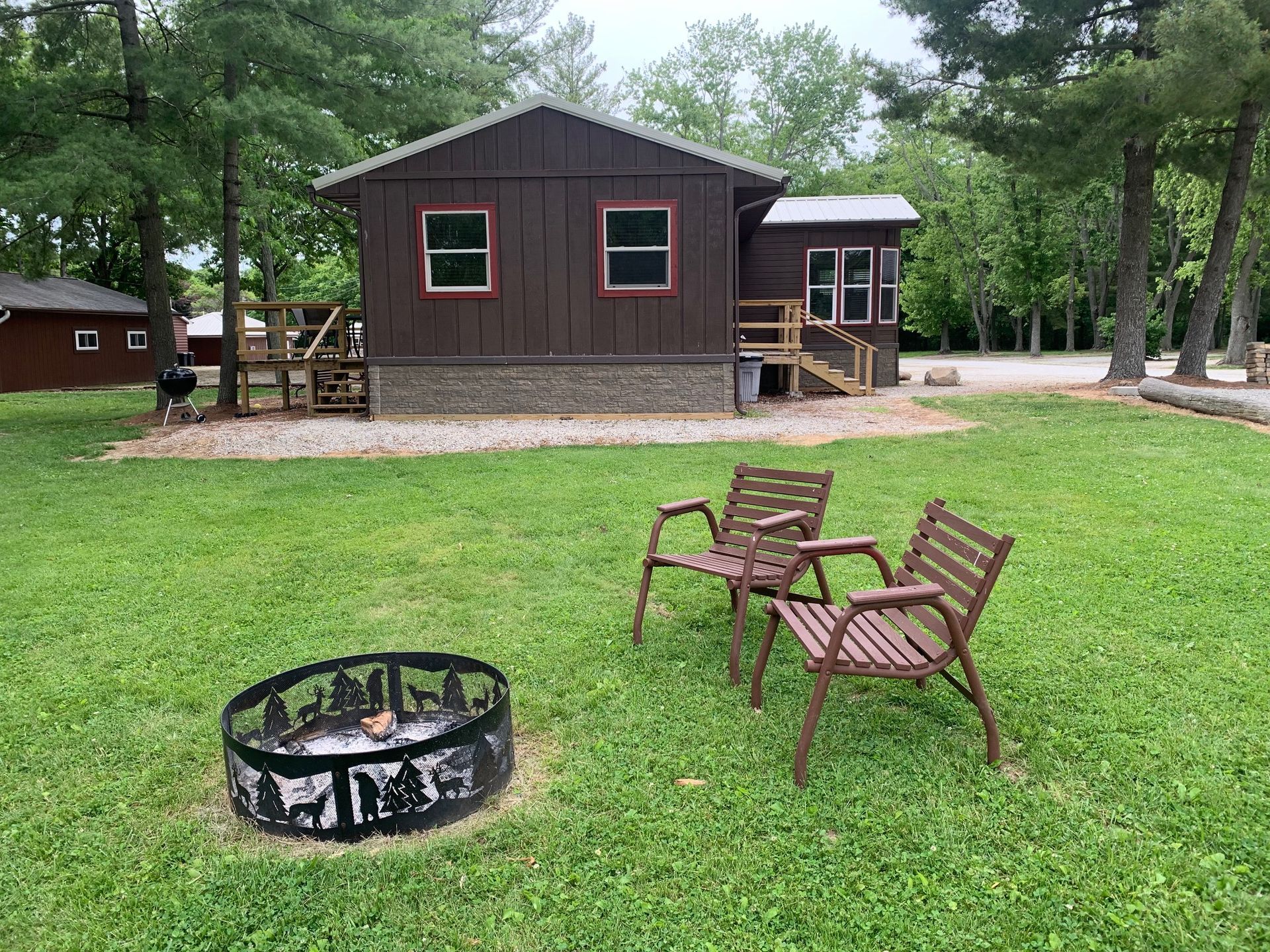 Brown cabin with two chairs and fire pit in a grassy yard.
