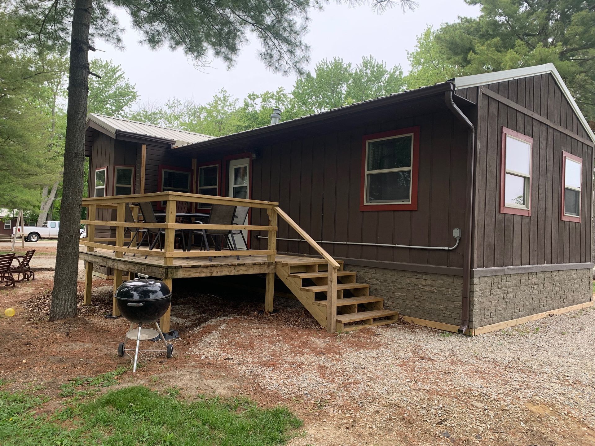 Brown cabin with deck, stairs, grill, and gravel yard.