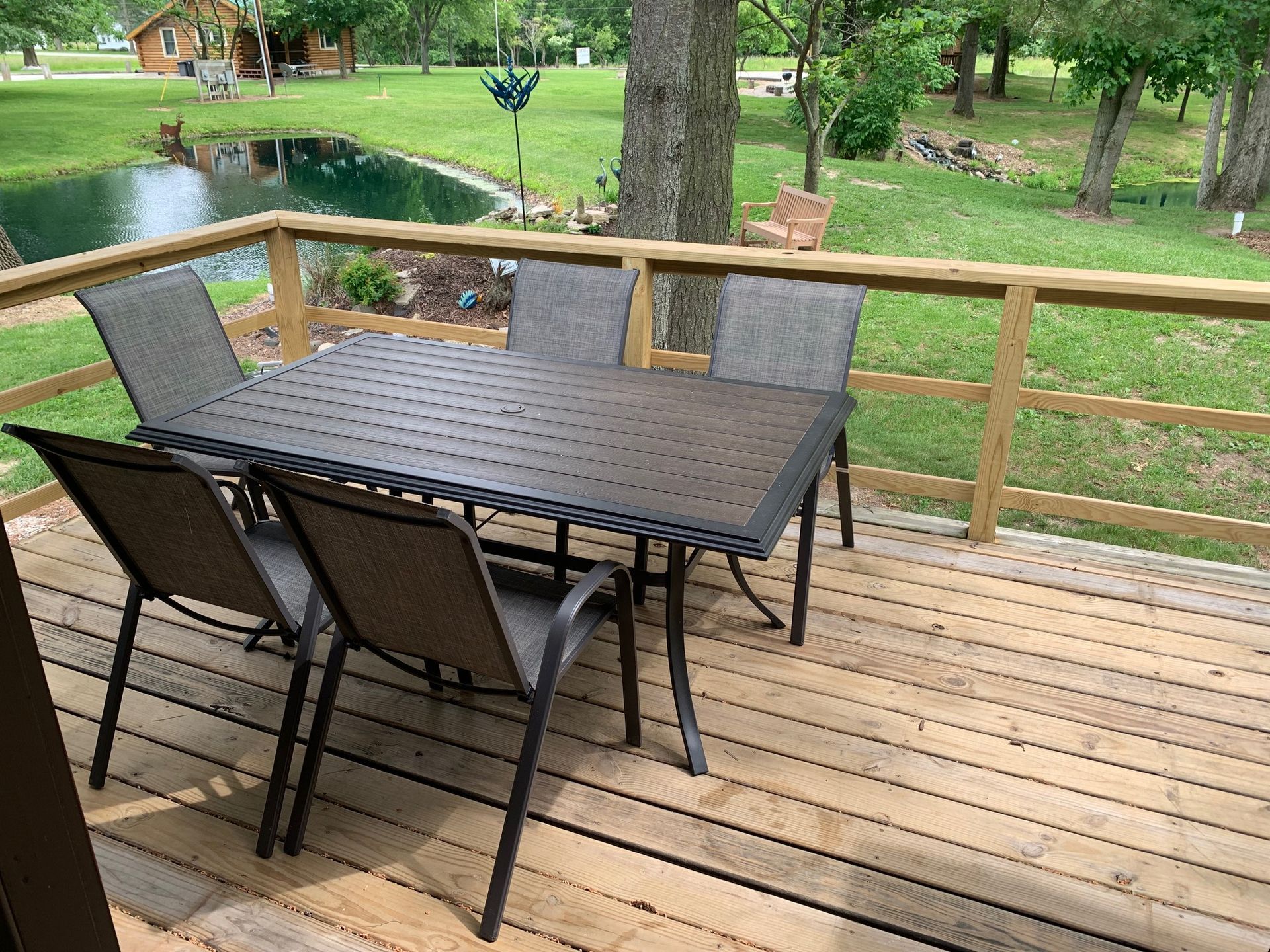 Deck with dark table and chairs overlooking a pond and yard.