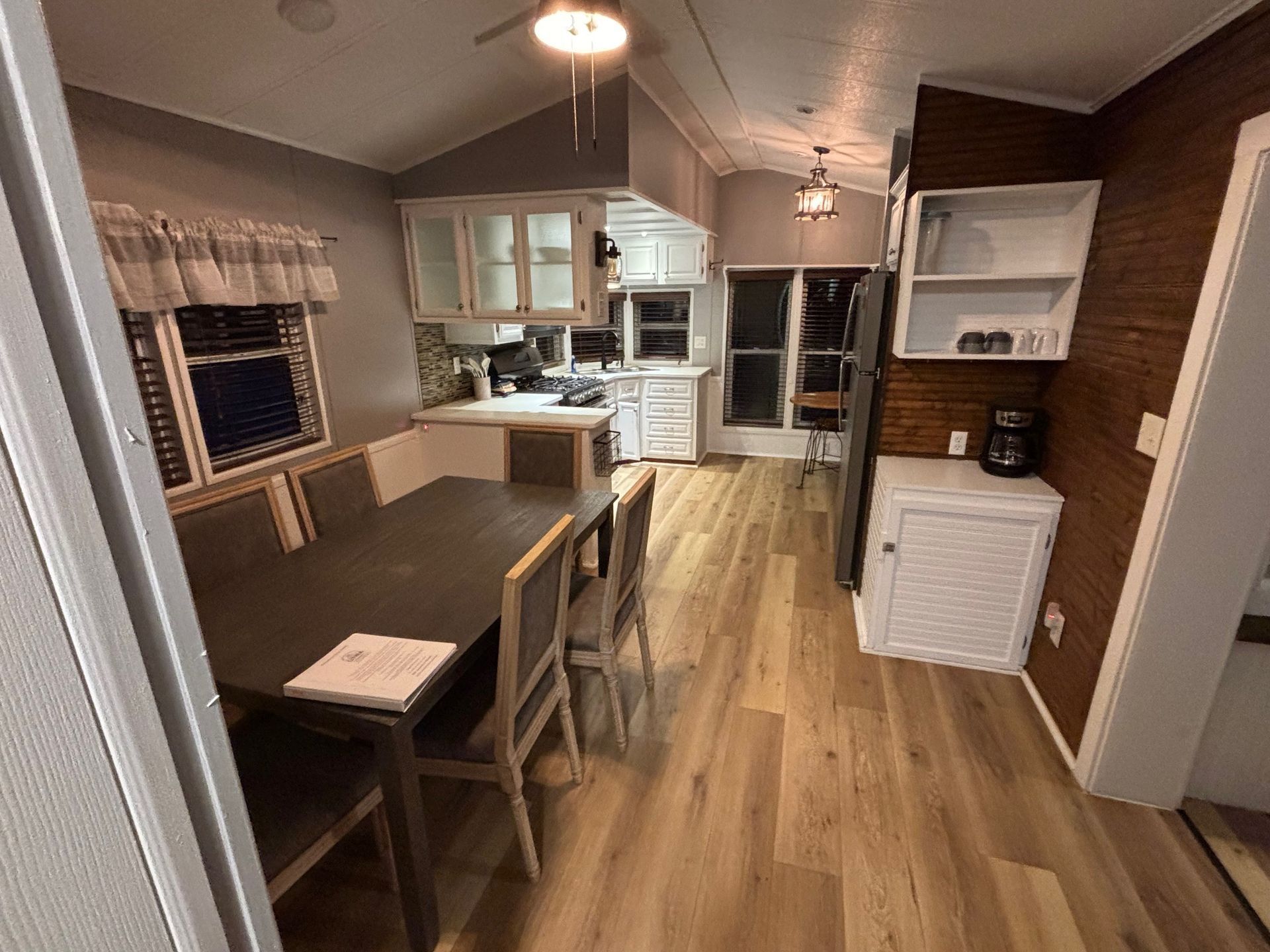 Dining area and kitchen inside a home a long table, chairs, white cabinets, and wood-look flooring.