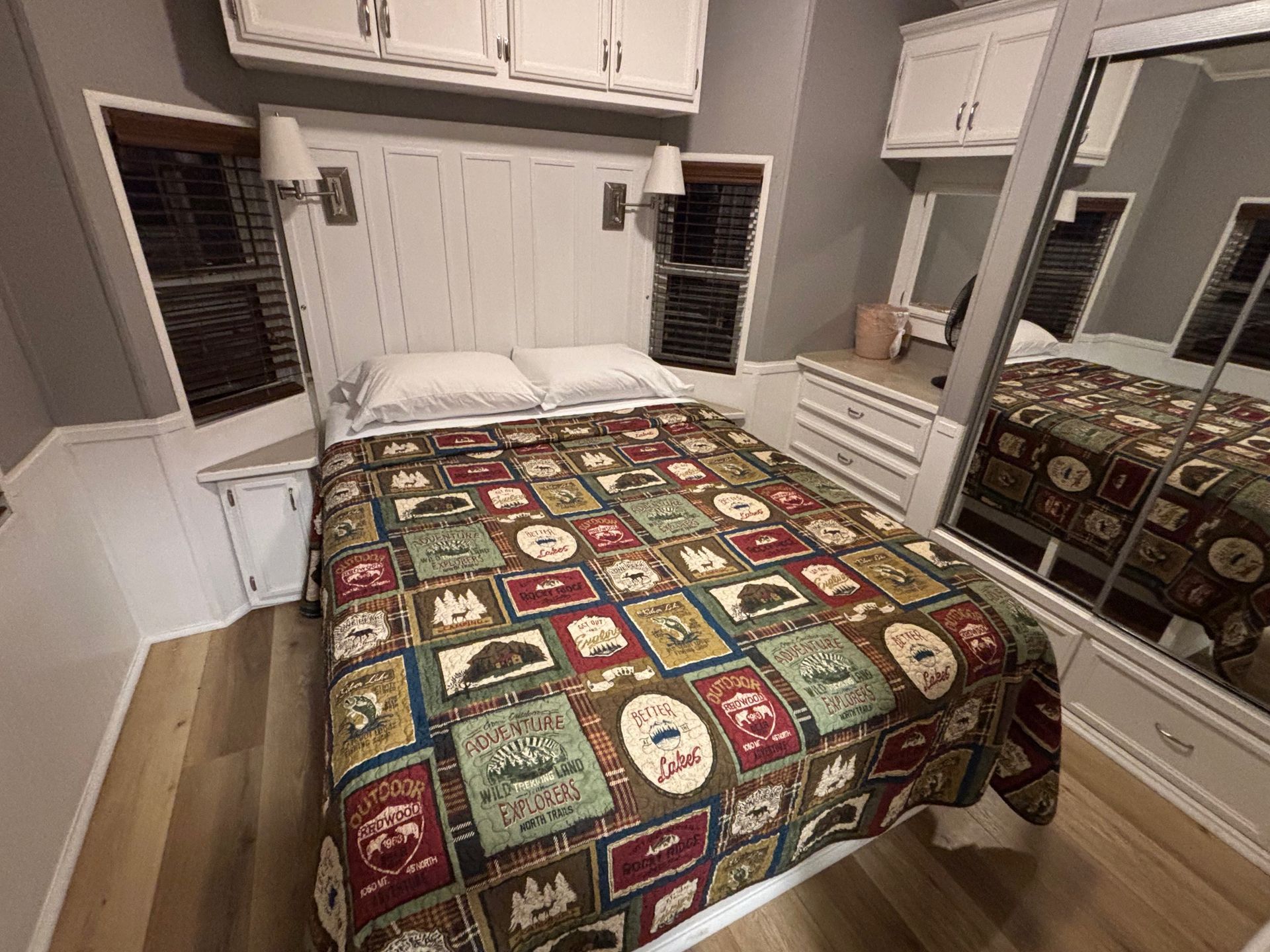 Bedroom with queen bed and overhead storage wooden headboard and light-colored walls.