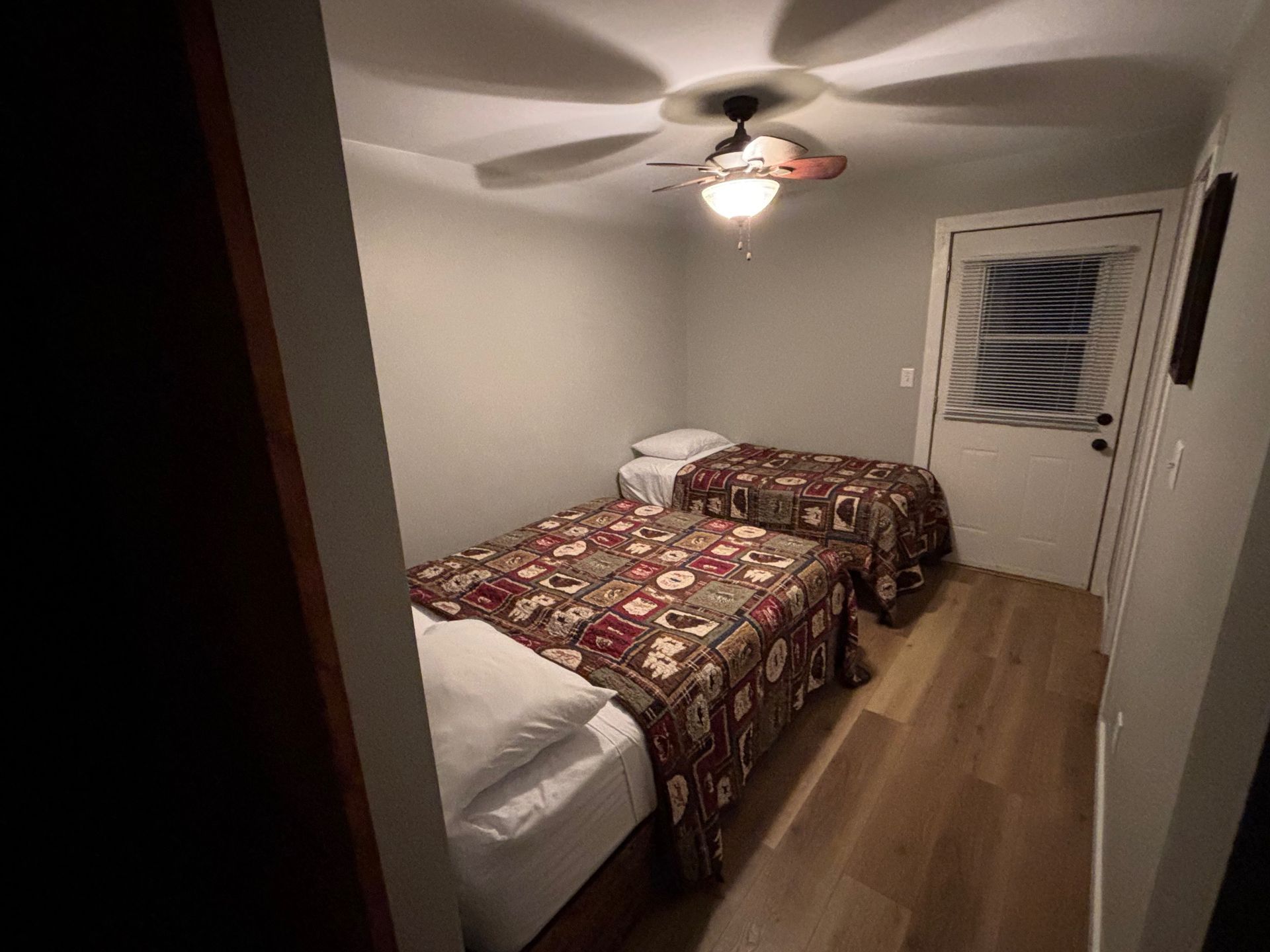 Two twin beds in a room with a ceiling fan, a door, and wood flooring.