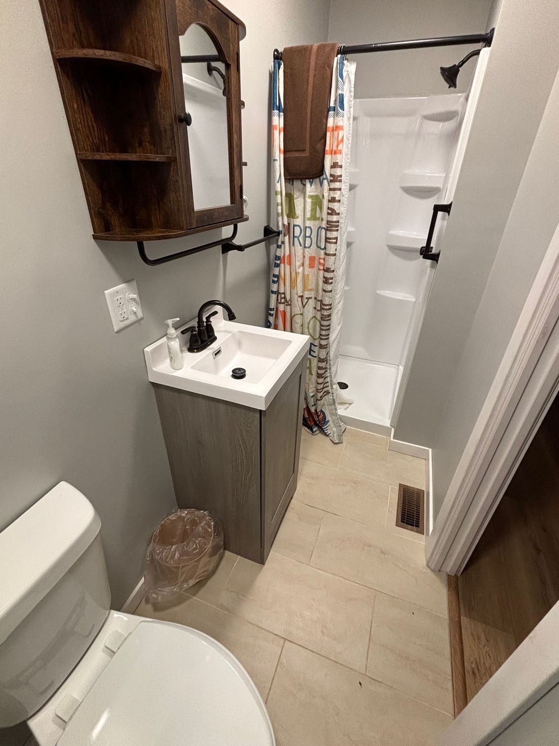 Small bathroom with a toilet, sink, and shower. Gray walls, light-colored floor.