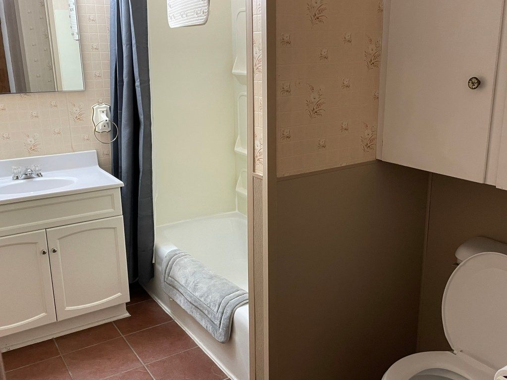 Small bathroom with a white vanity, shower curtain, floral wallpaper, and visible toilet.
