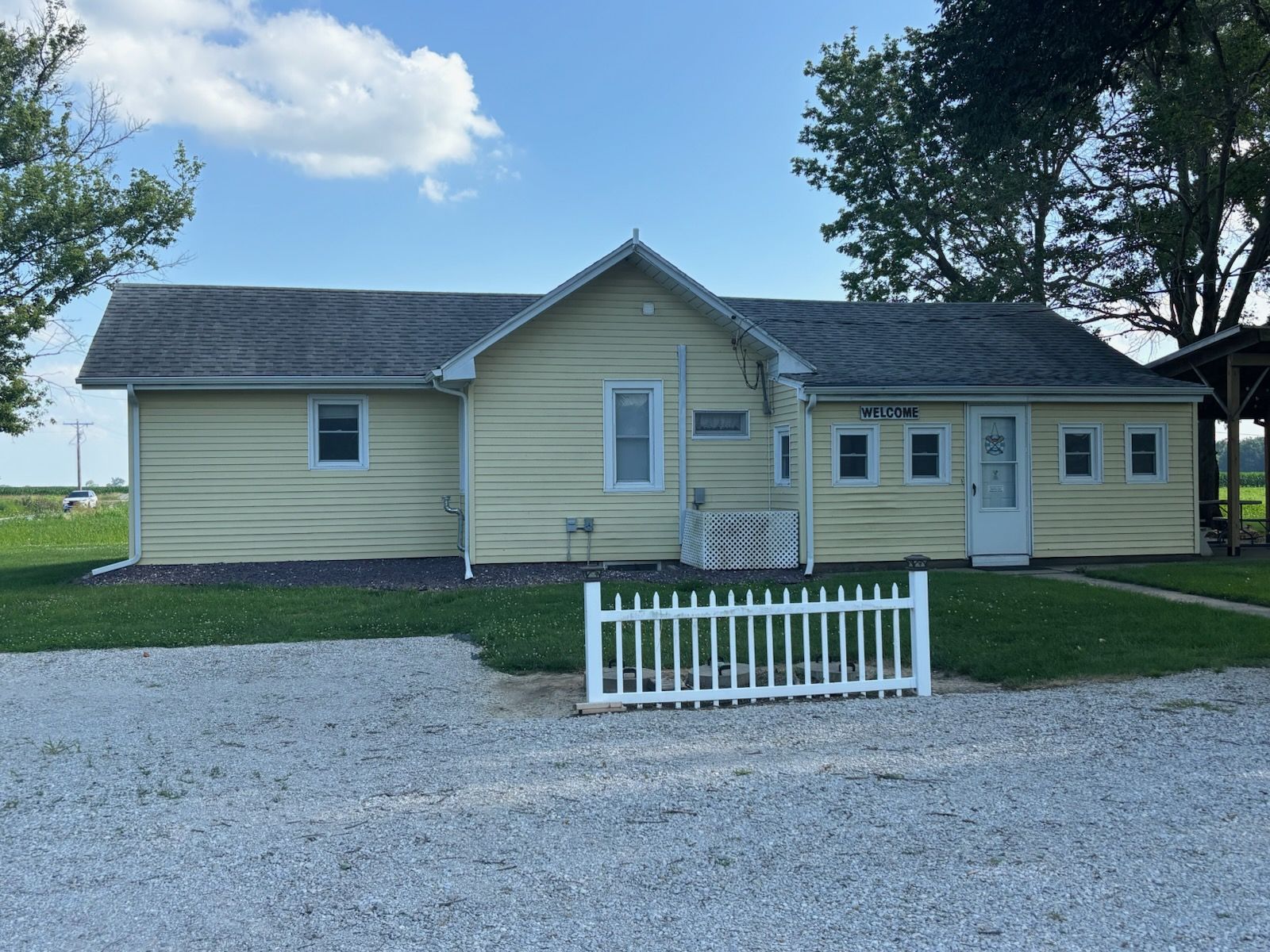 Yellow single-story house with white trim, gravel driveway, and small white fence in front