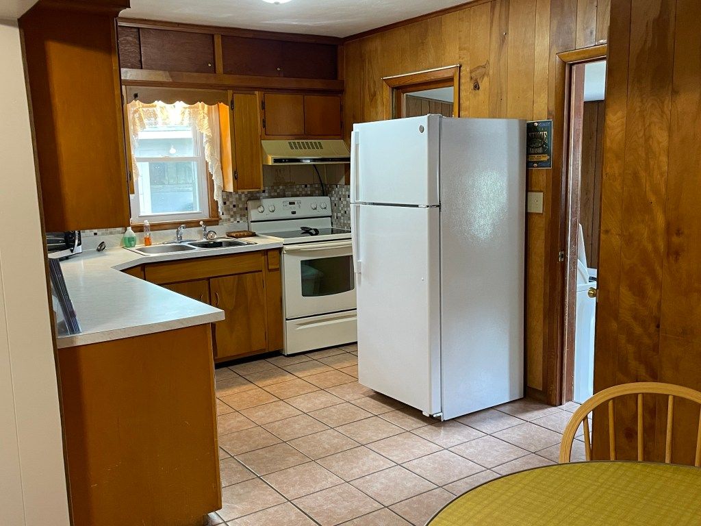Small wood-paneled kitchen with white refrigerator, stove, sink, and tiled floor.