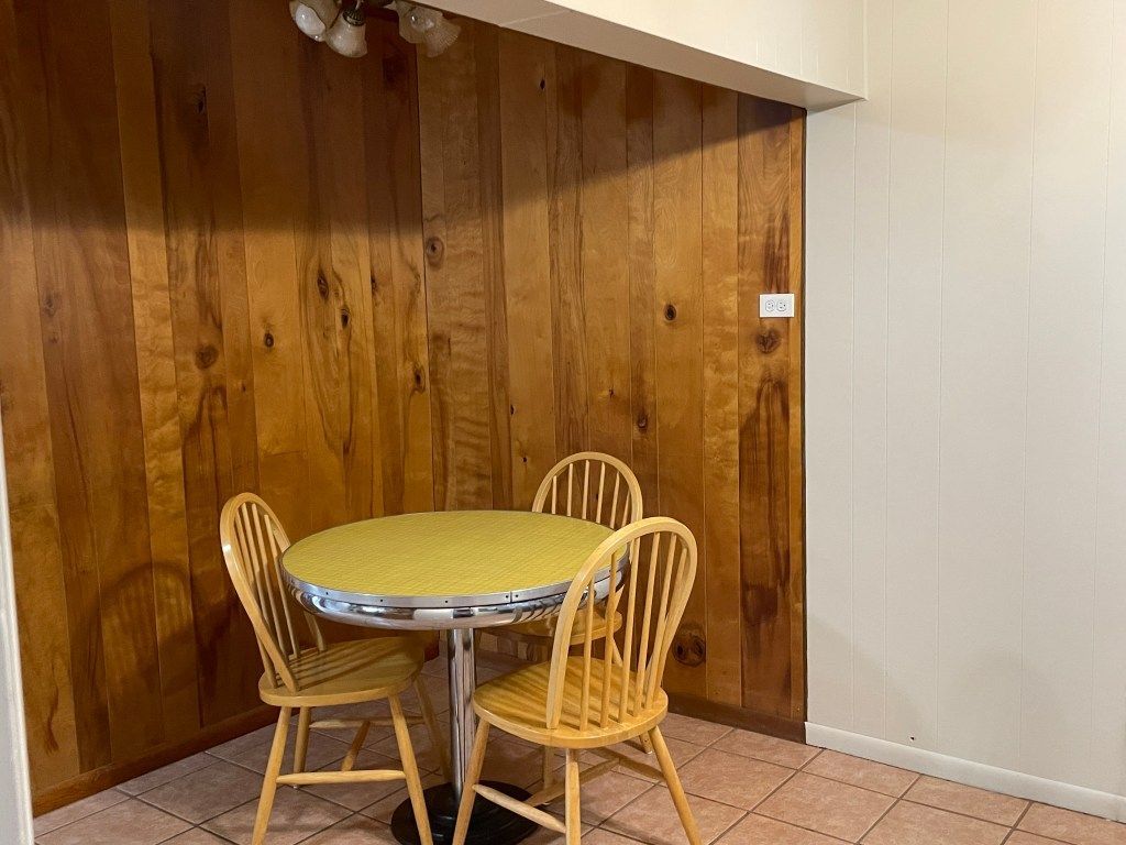 Small dining nook with a round table and three wicker chairs against wood-paneled walls