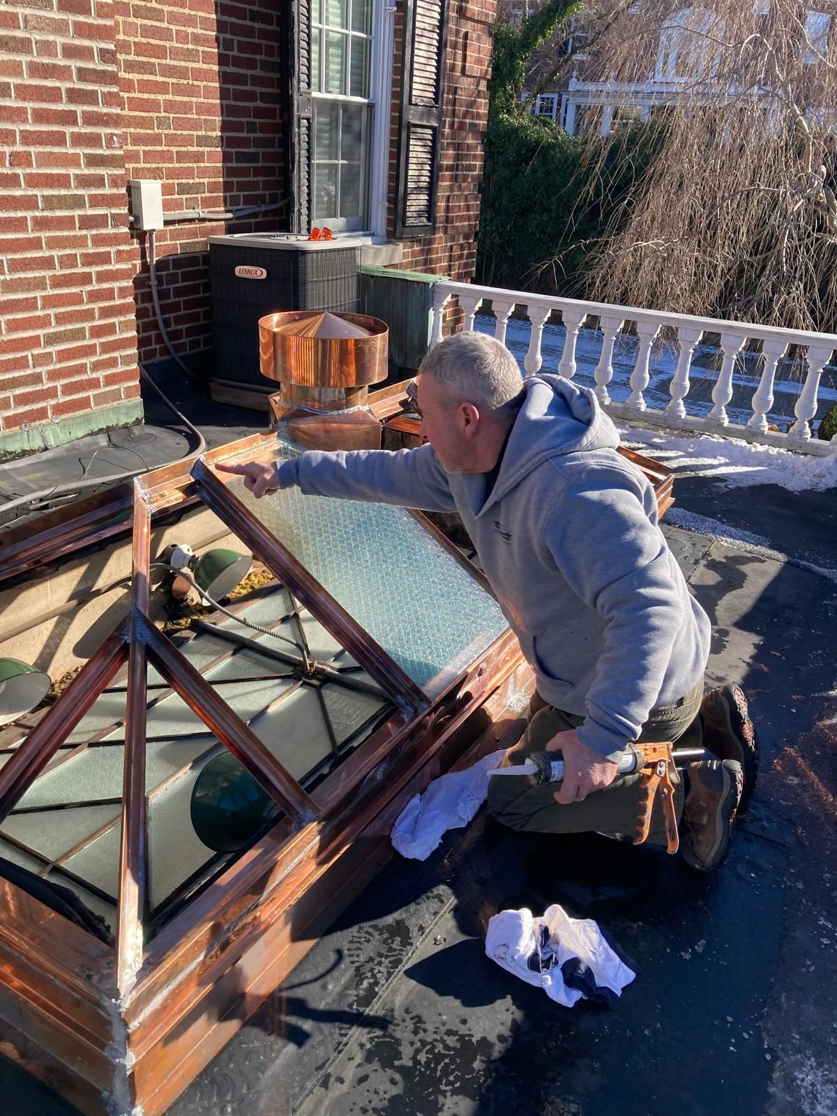 A man is kneeling down on a roof working on a window.