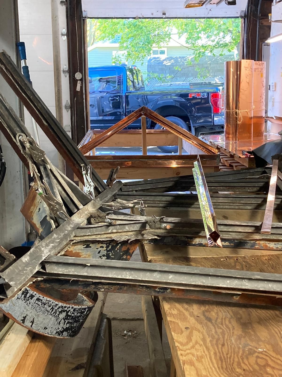 A bunch of metal pieces are sitting on top of a wooden table in a garage.