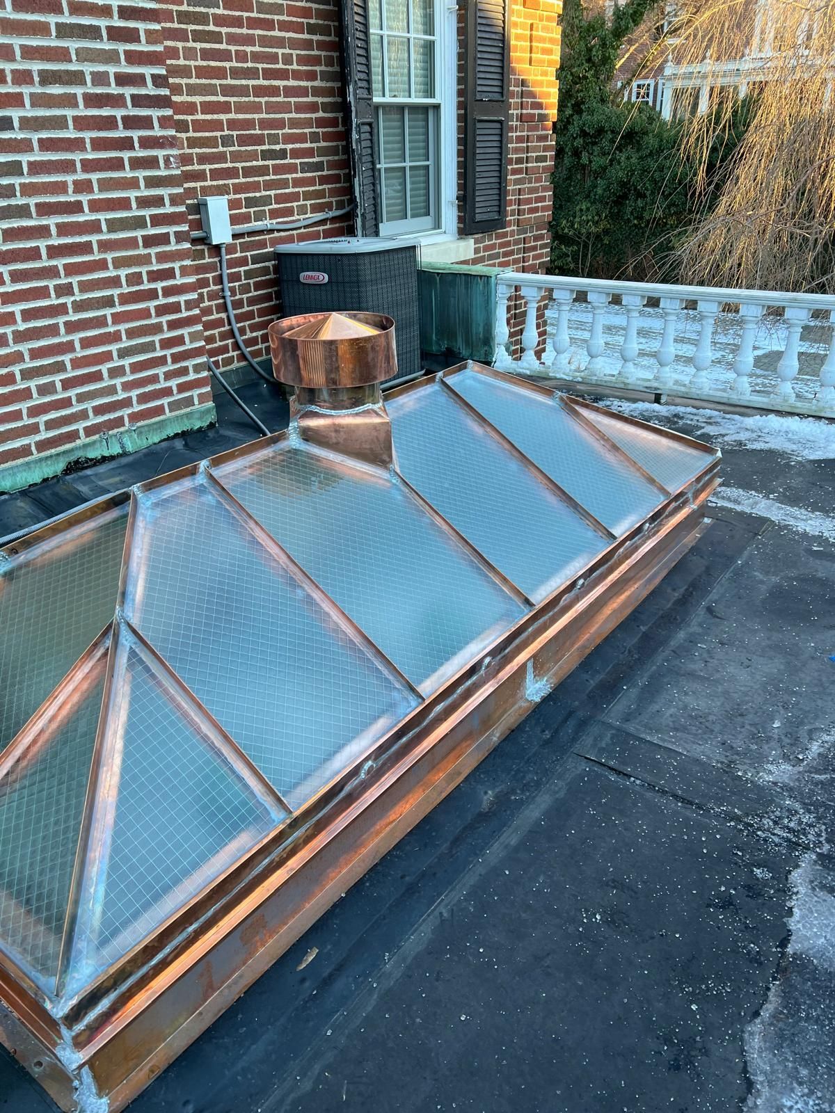 A copper skylight is sitting on top of a roof next to a brick building.