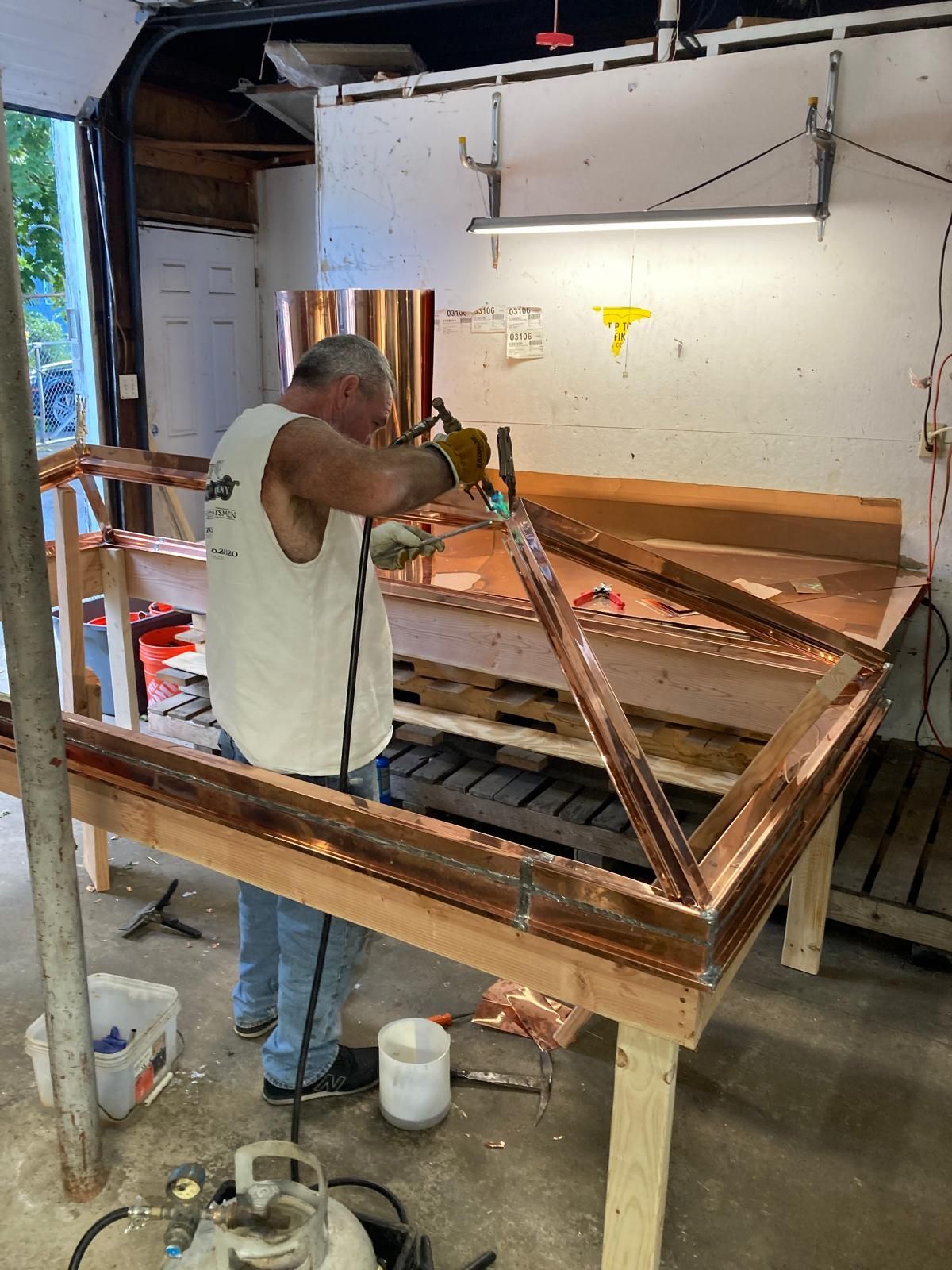 A man is working on a piece of copper in a garage.