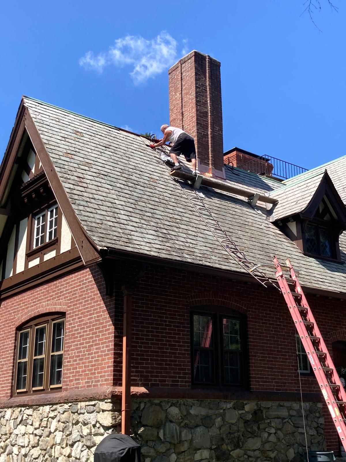 A man is working on the roof of a brick house.