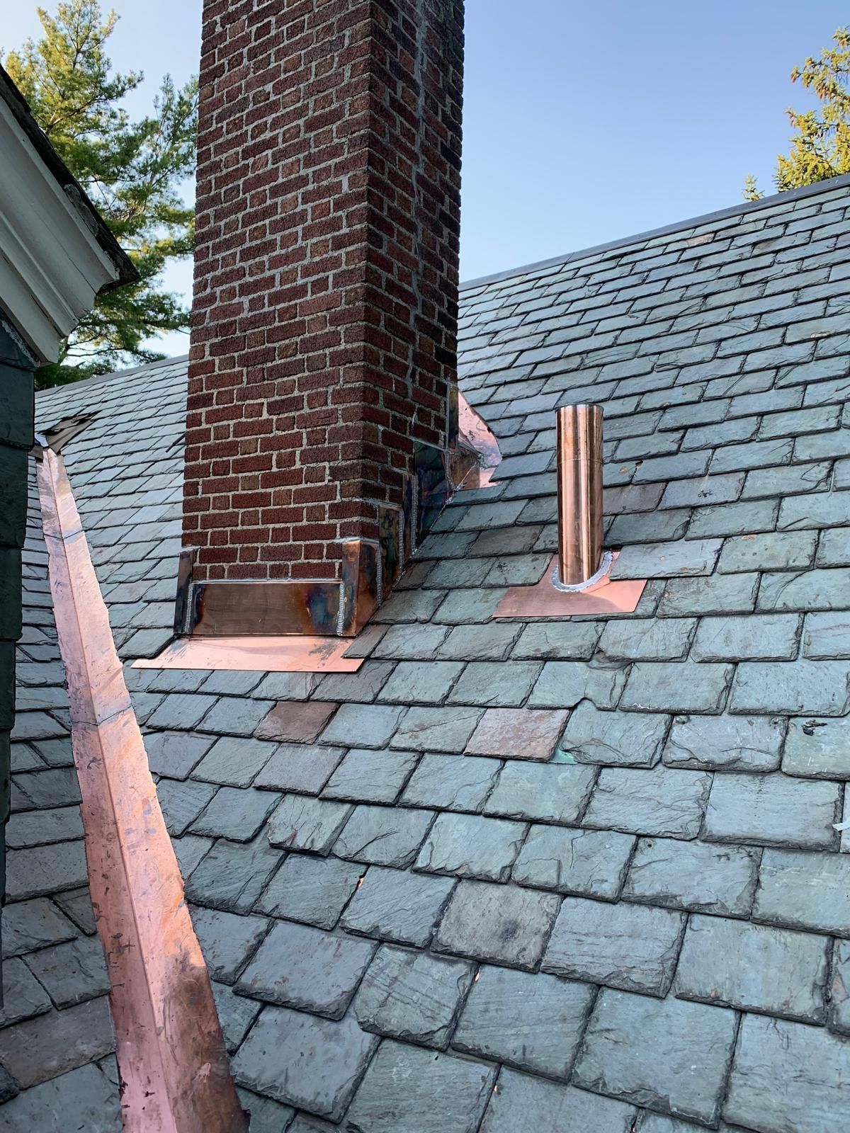 A brick chimney is sitting on top of a slate roof.