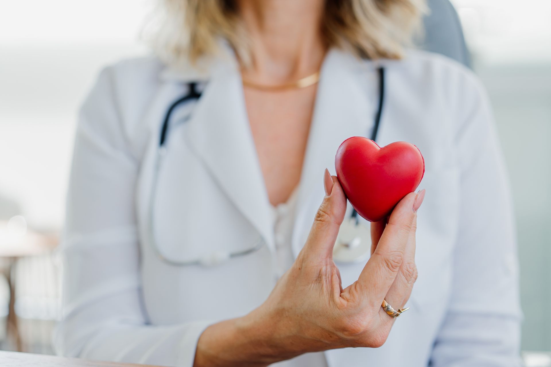Doctor in white coat holding a red heart; stethoscope around neck.