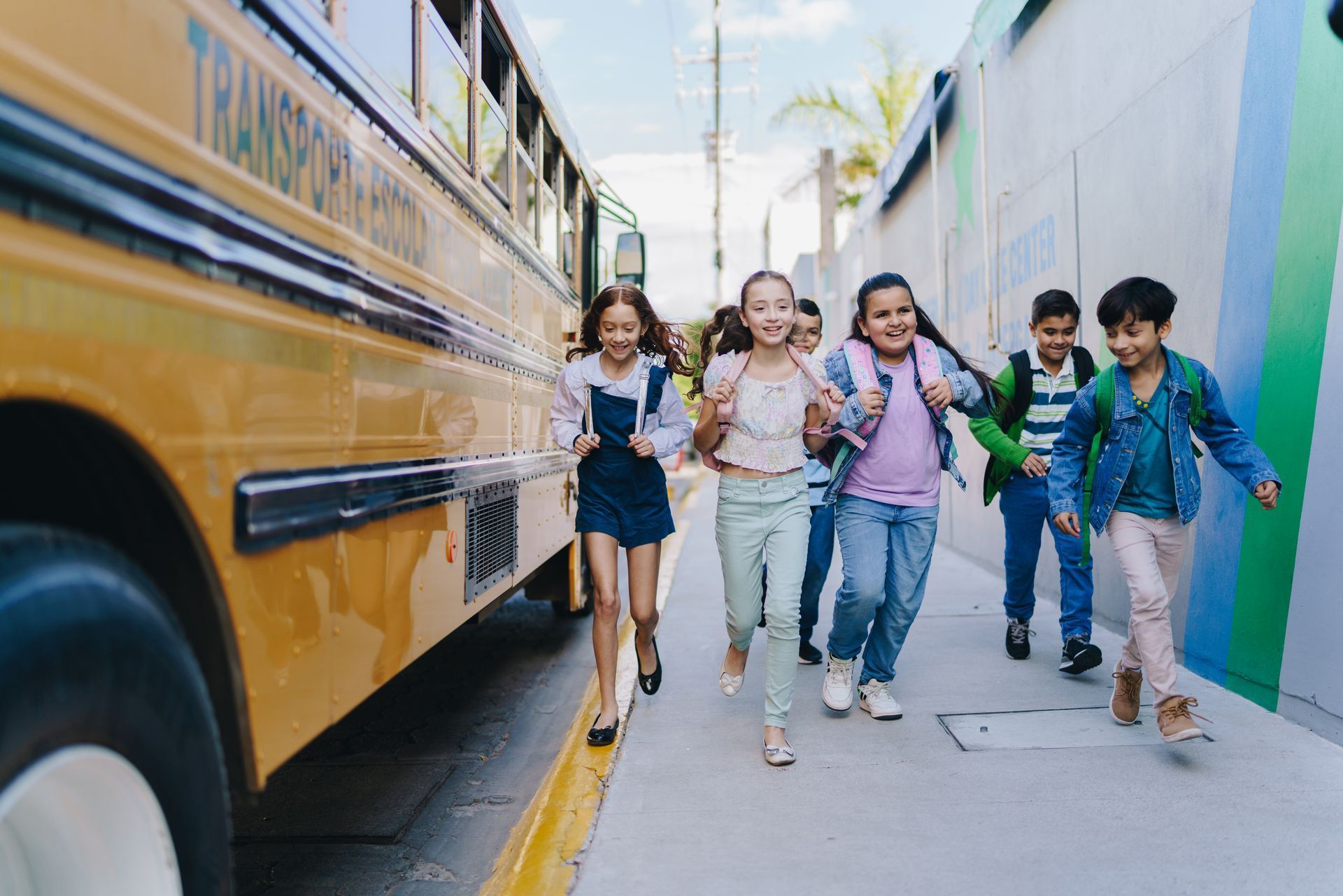 School children running excitedly off a yellow school bus.