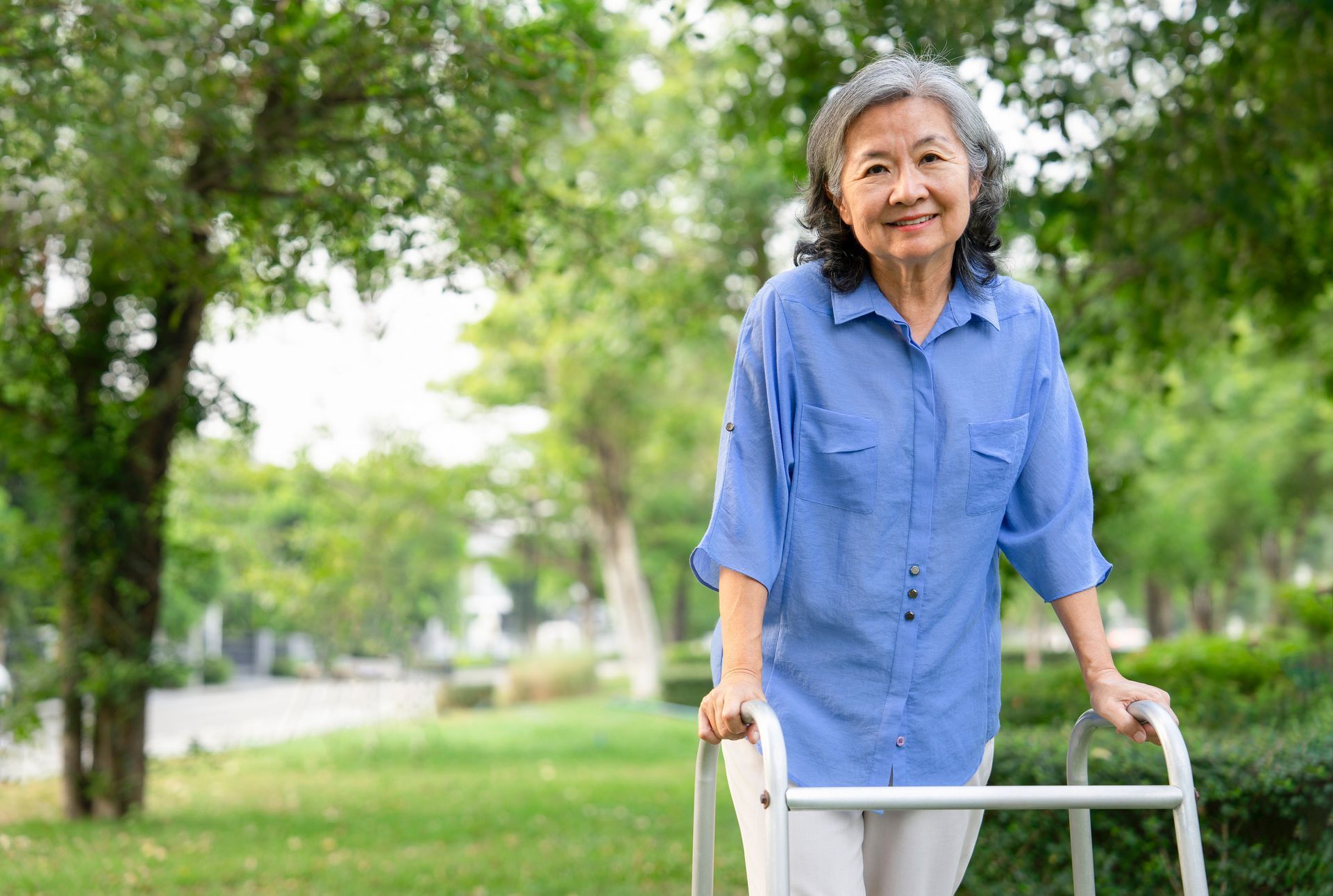 Smiling elderly woman in blue shirt using a walker in a park.