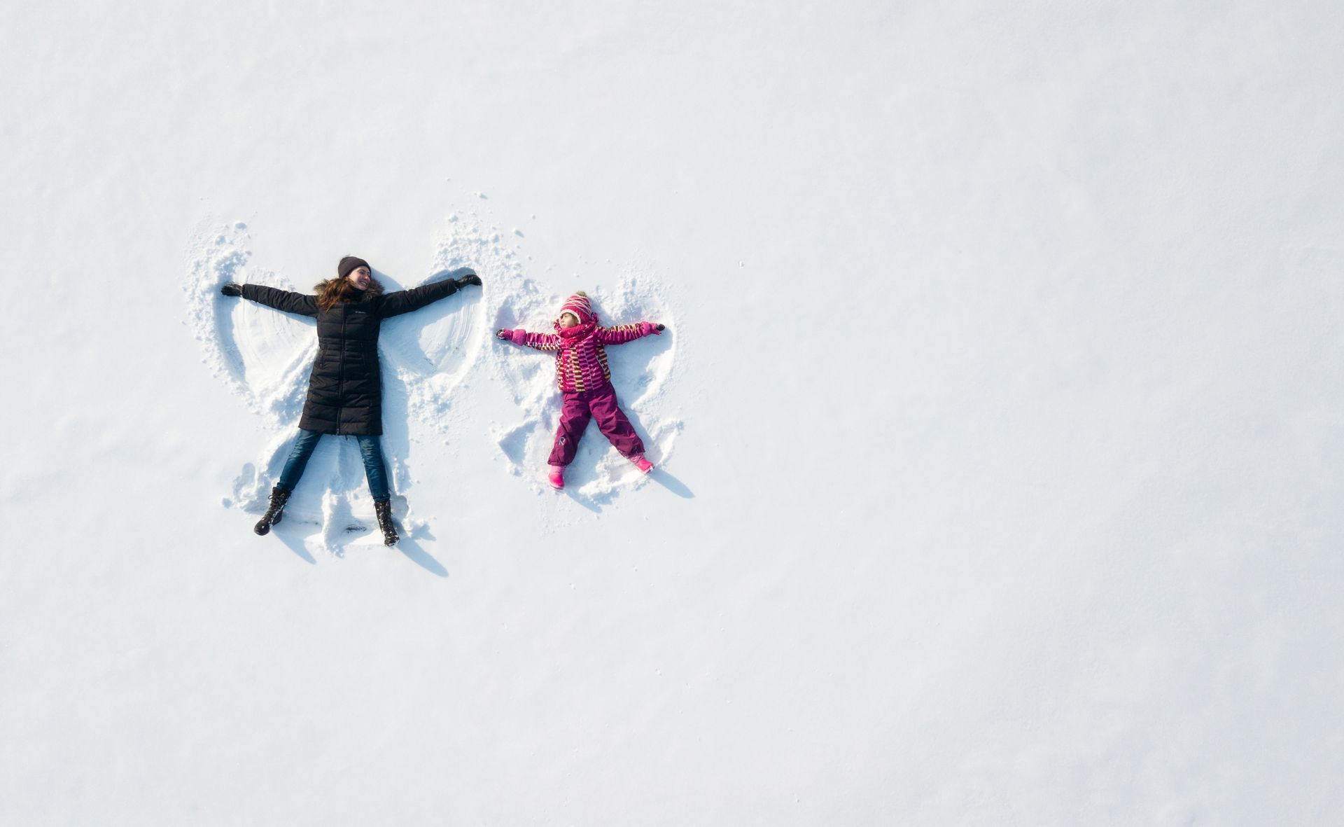 A person and child making snow angels in a field of white snow.