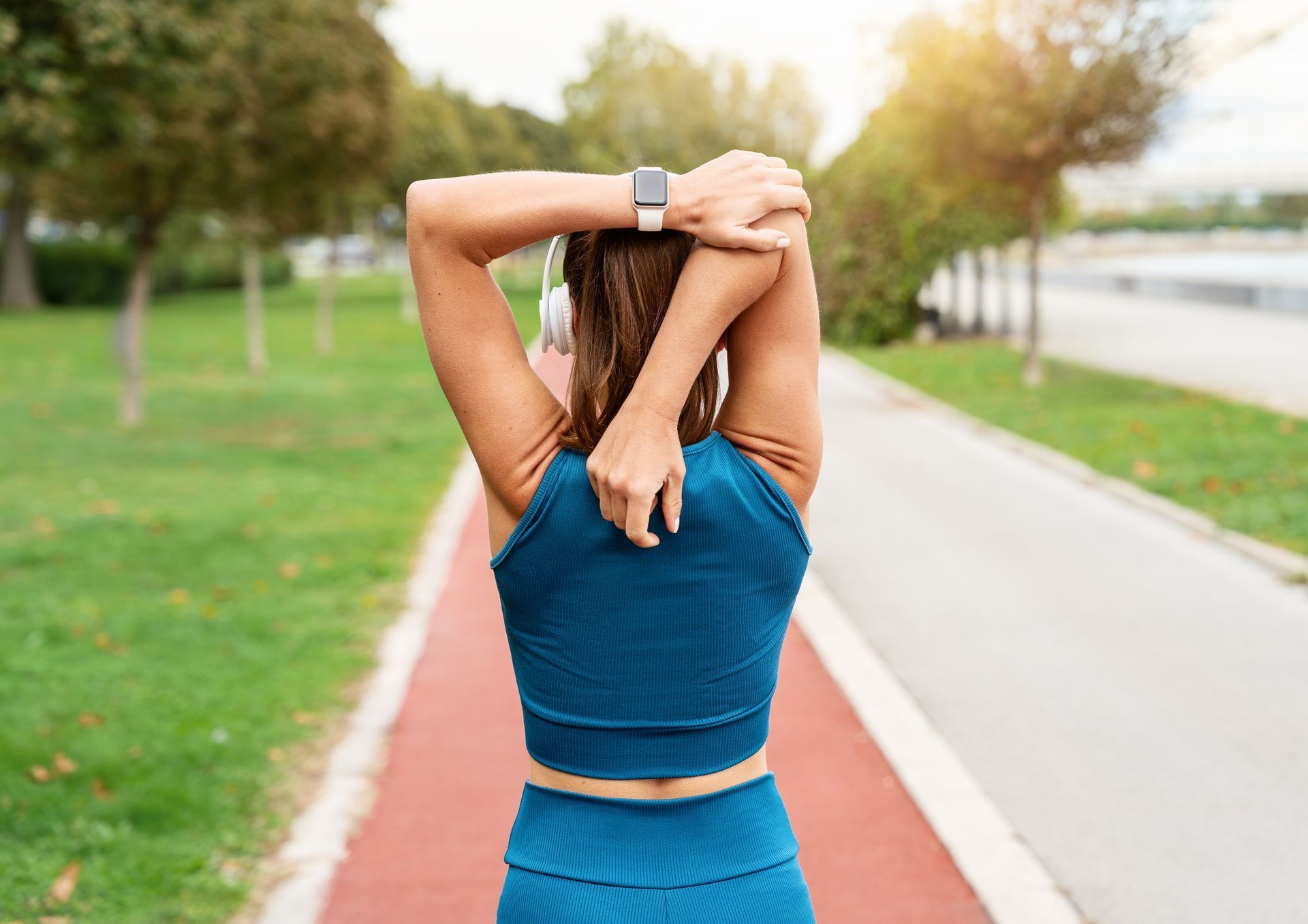 Woman stretching arms behind back on a red track in park.