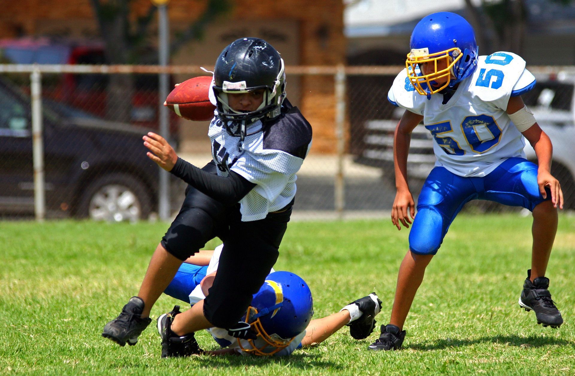 Youth football players in action on a green field, one running with the ball, another tackling, and a third looking on.