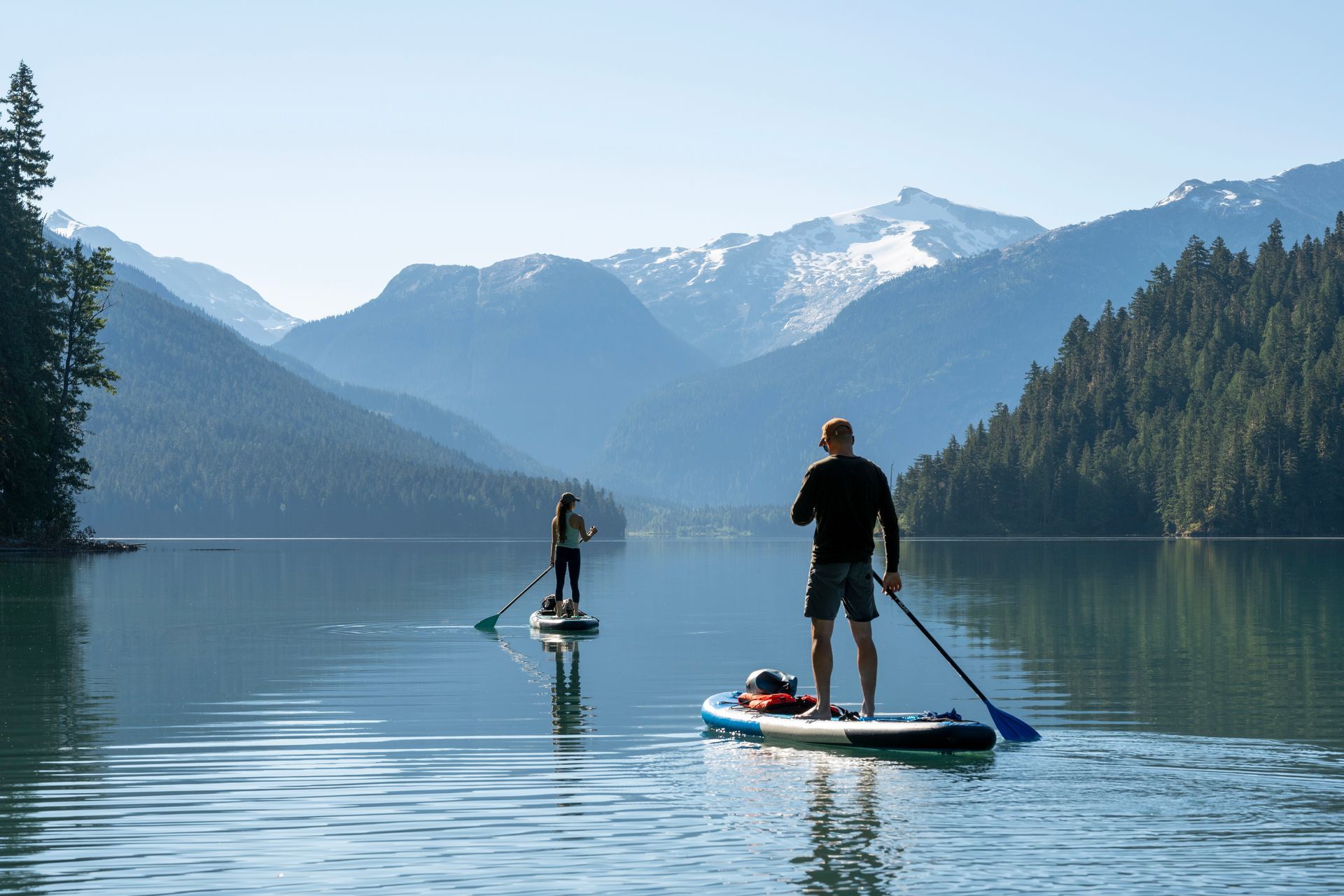 Two people paddleboarding on a lake with mountains in the background.