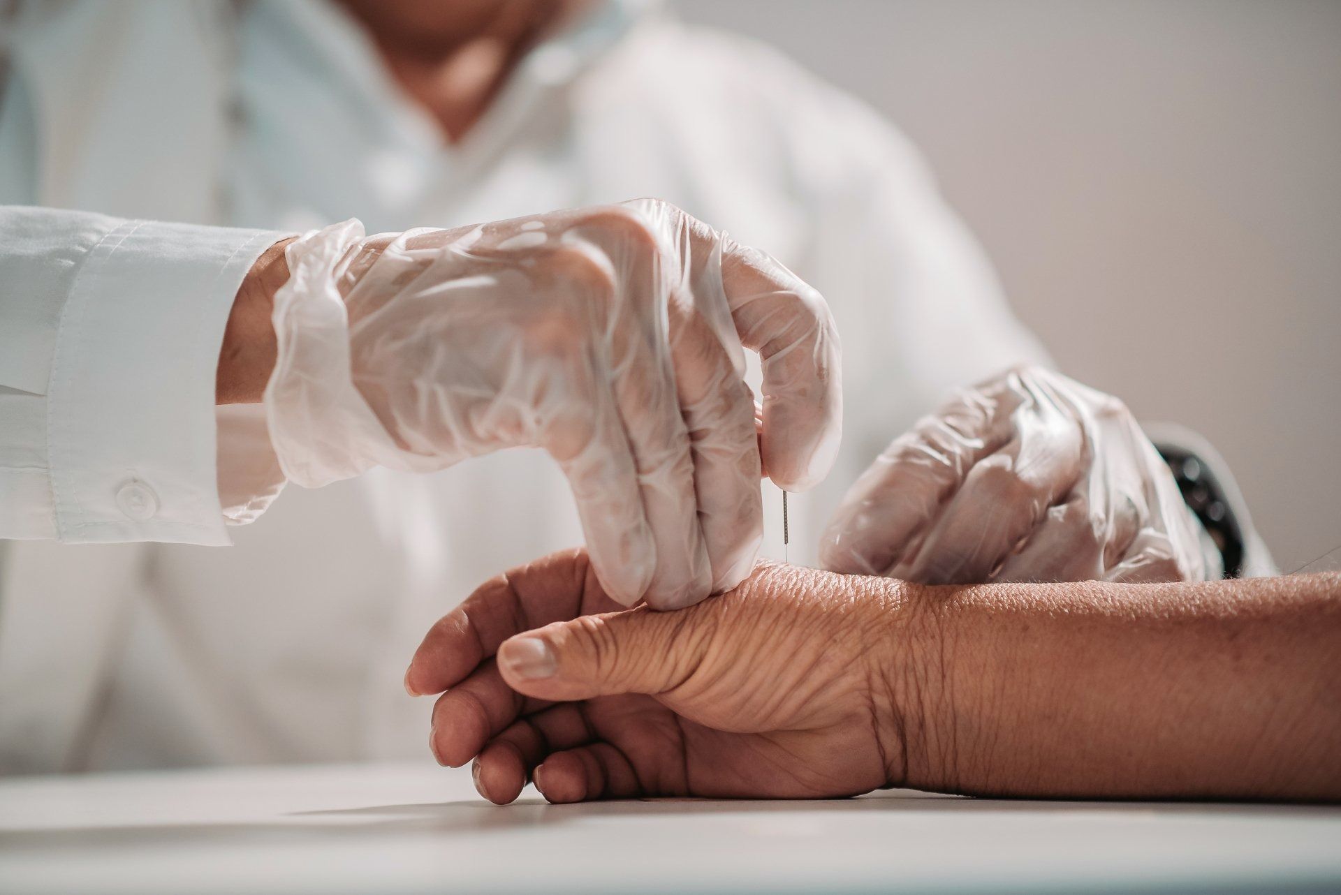 Doctor's gloved hands touching a patient's wrist in a medical setting.
