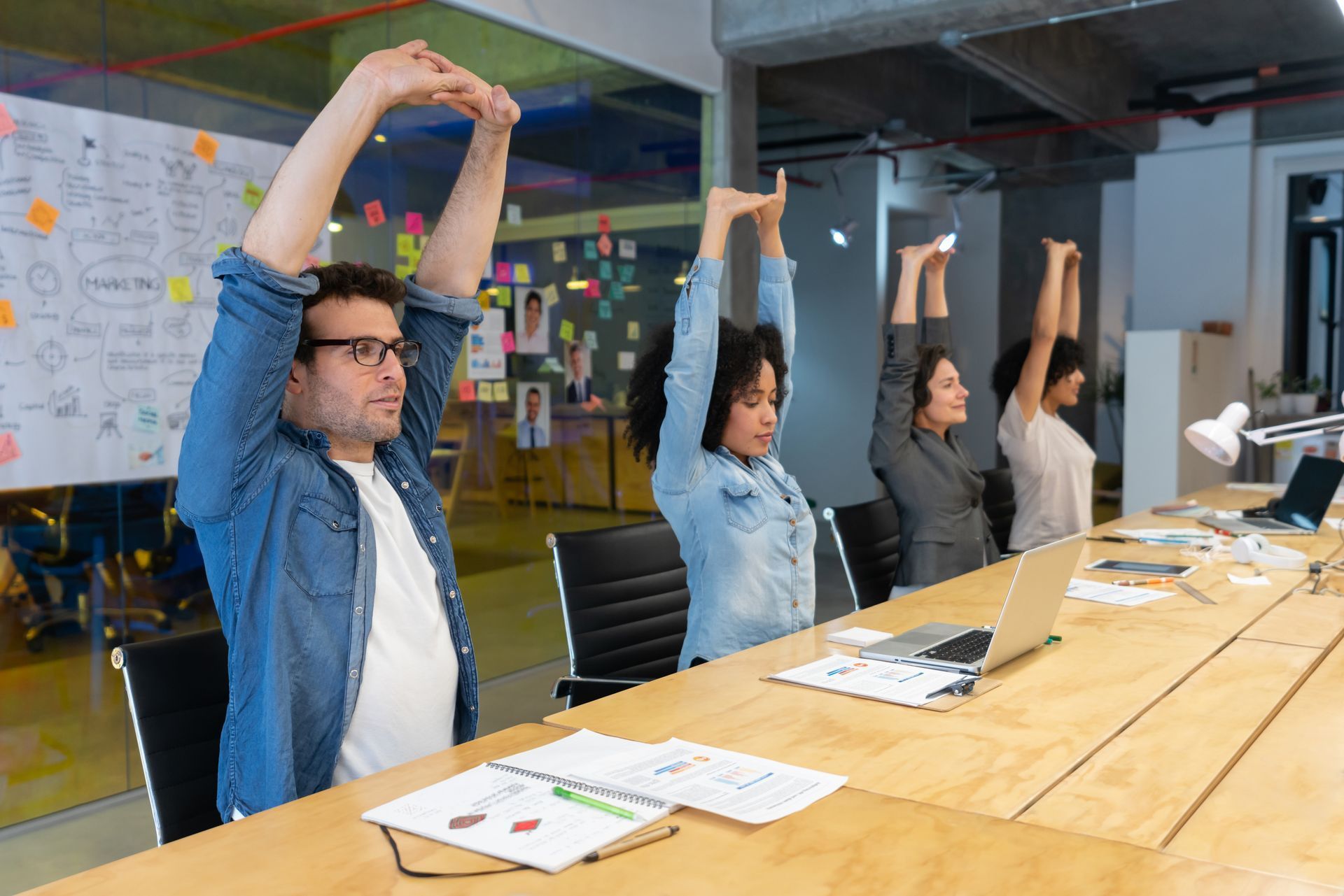 Four office workers stretching arms above heads at a table.