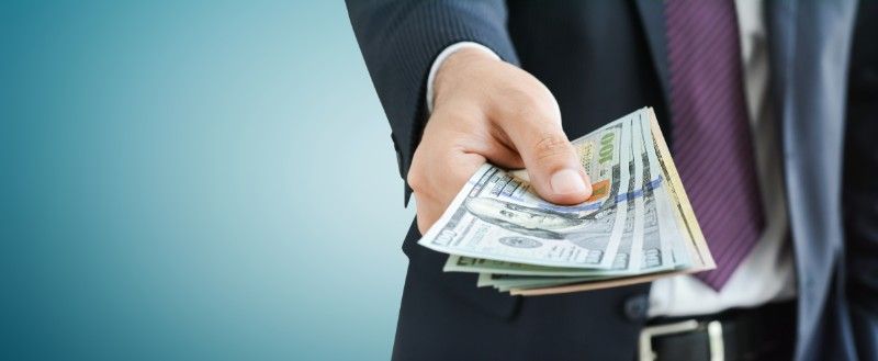 A man in a suit and tie is holding a bunch of money in his hand.