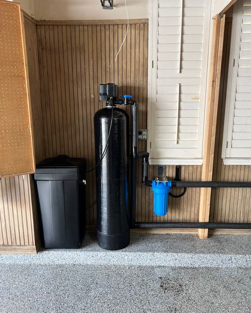 A water filter is sitting in a garage next to a trash can.