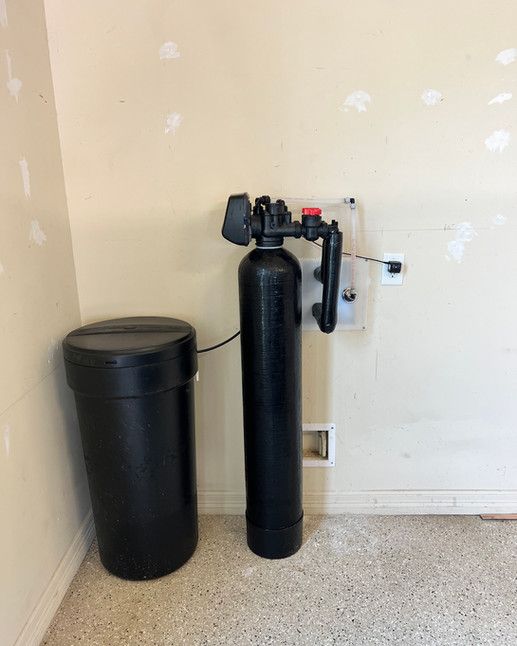 A water softener is sitting next to a trash can in a room.