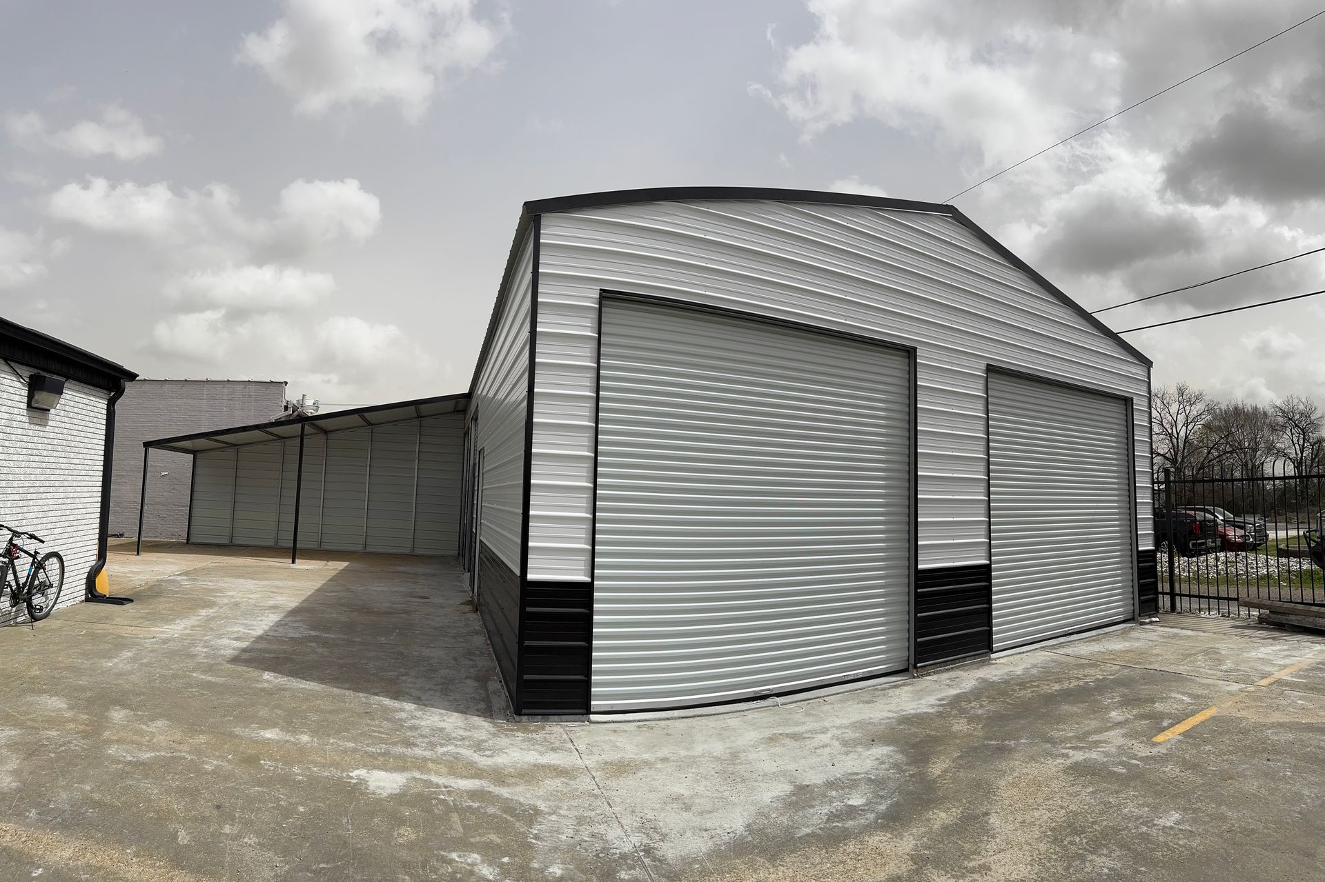 A large metal building with two garage doors is sitting in a parking lot.