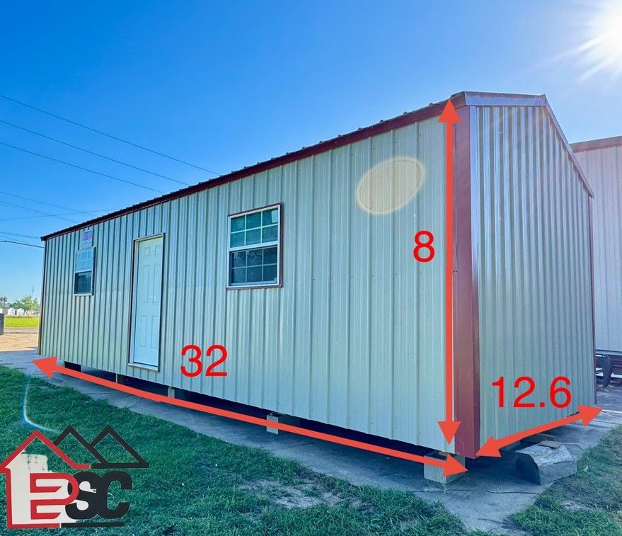 A shed with measurements on the side of it is sitting in the grass.