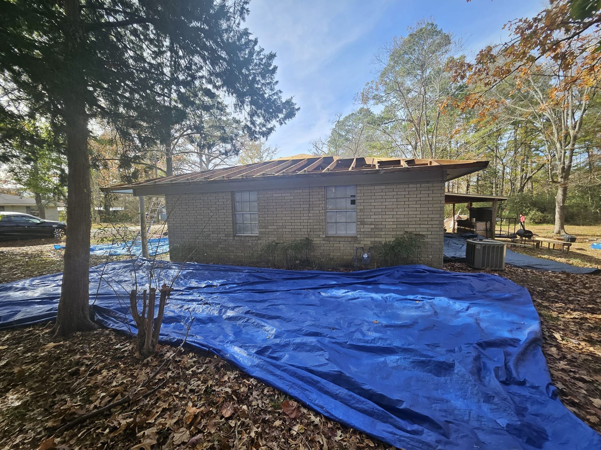 A blue tarp is covering a wooden house in the woods.