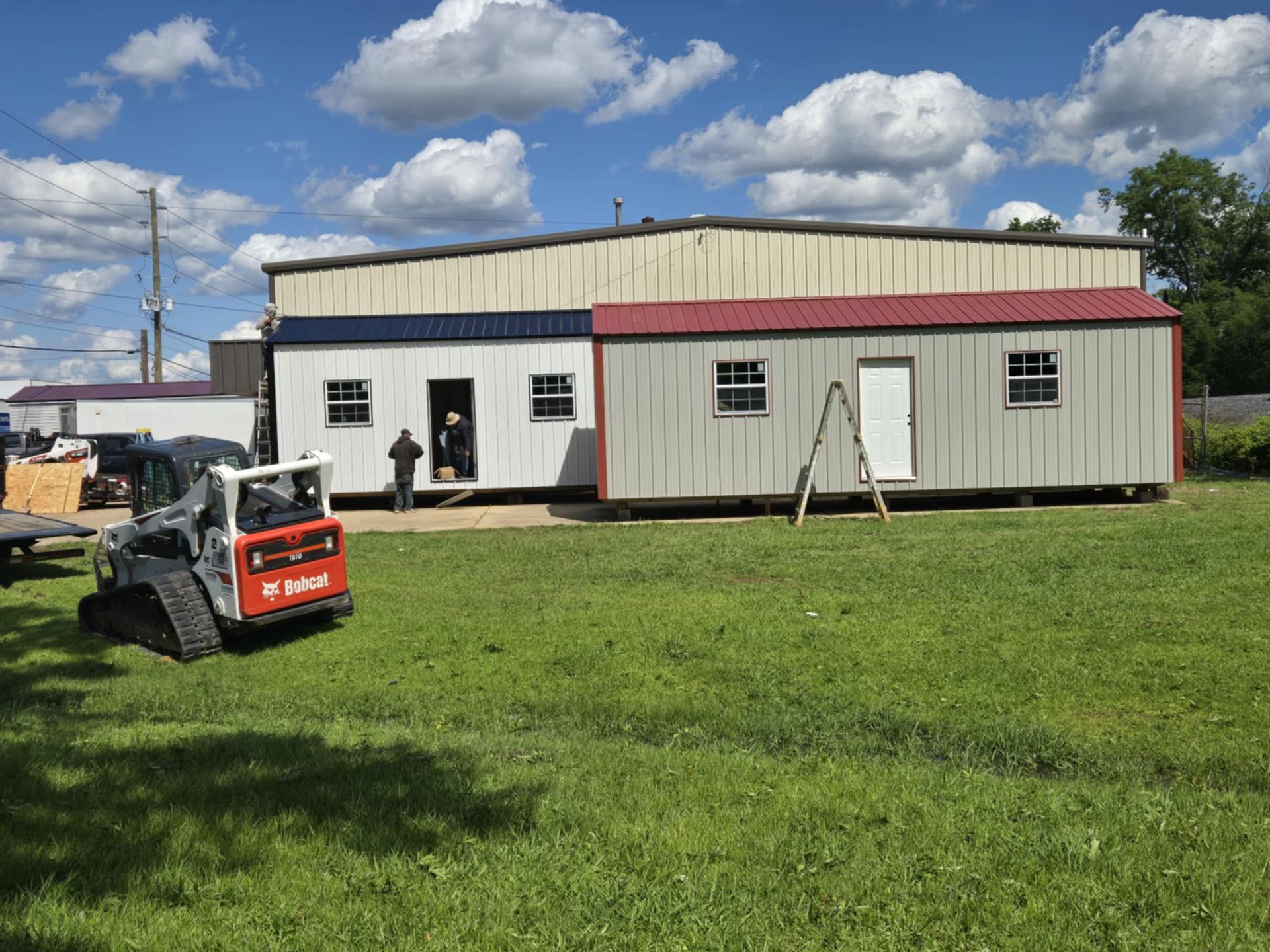 A bobcat is parked in front of a large building in a grassy field.