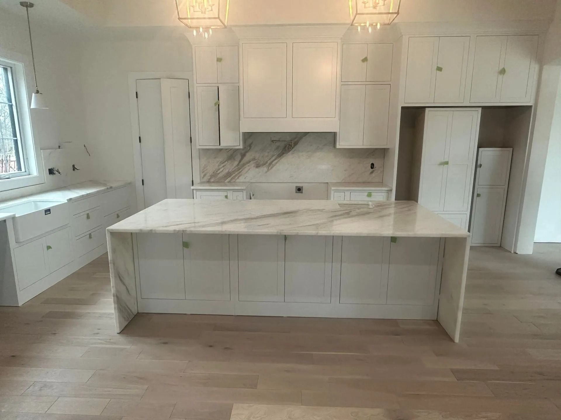 White kitchen with marble countertops, cabinets, and island. Natural light floods the space.
