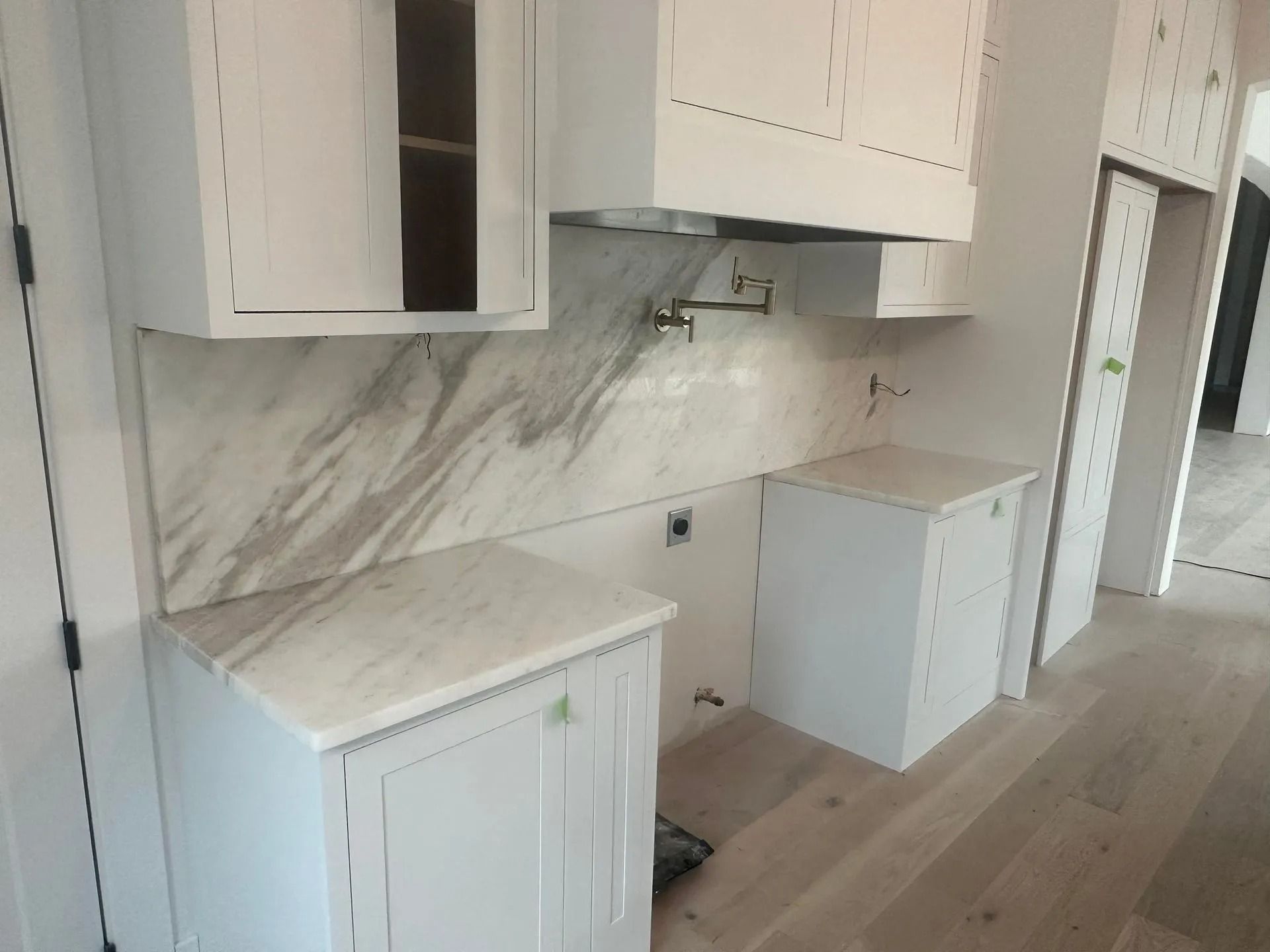 Kitchen cabinets with marble backsplash and countertops, under-construction with stainless steel range hood.