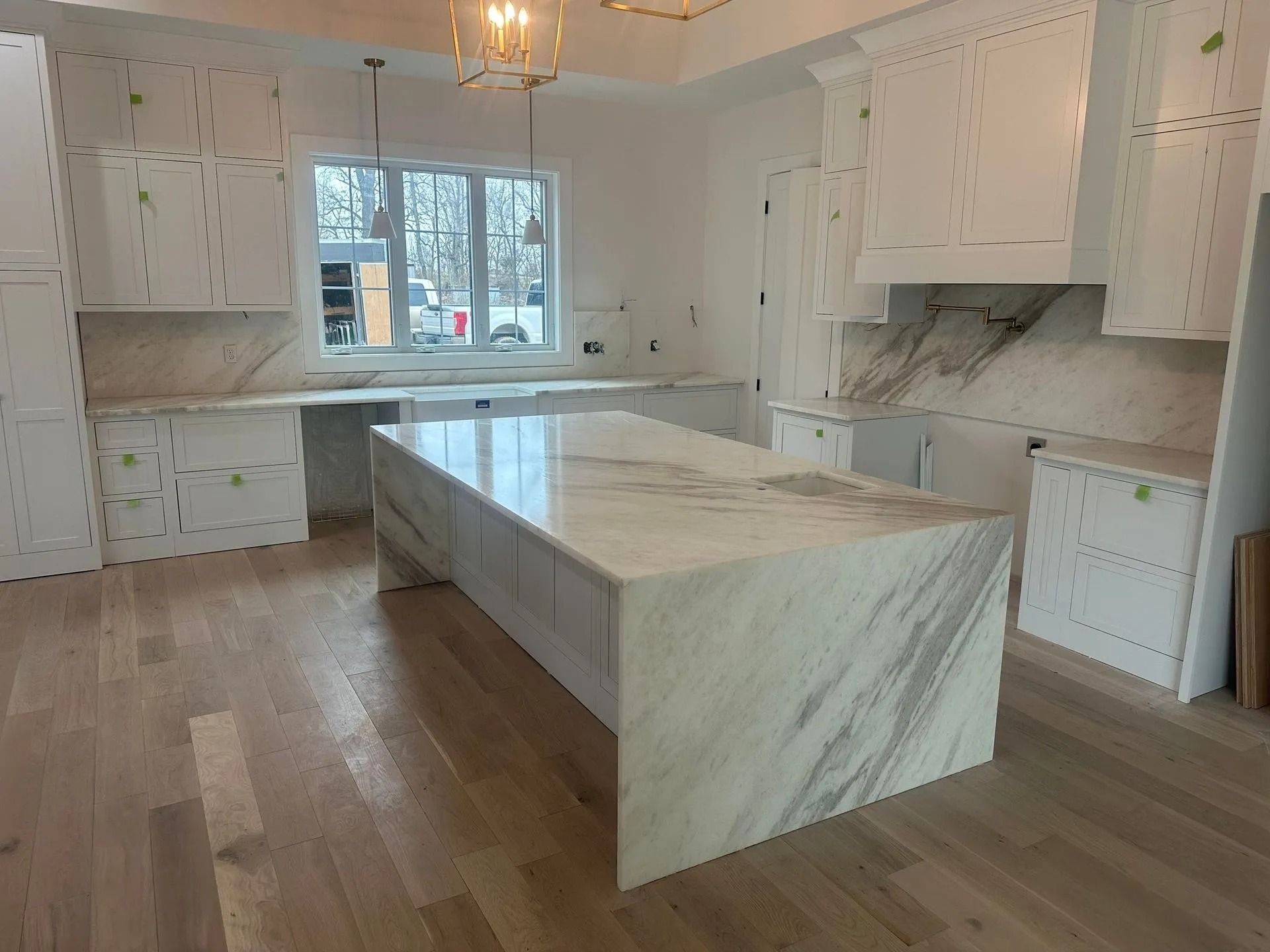 Modern kitchen with white cabinets, marble countertops, and island; light wood flooring.