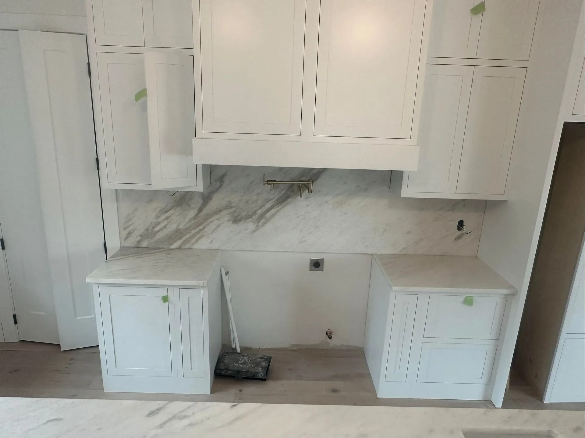 White kitchen cabinets and countertops with marble backsplash. Construction in progress.