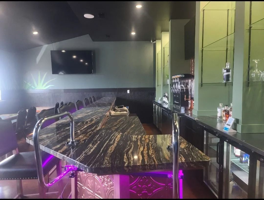 Bar interior with granite countertop, barstools, liquor bottles, and a mounted TV.
