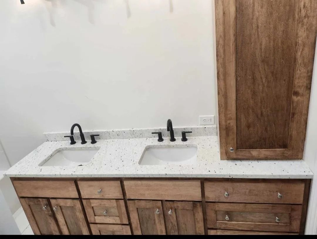 Bathroom vanity with two sinks, wooden cabinets, speckled countertop, and black faucets.
