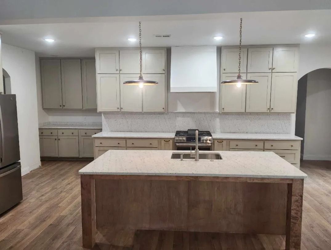 Kitchen with light-colored cabinets, white countertops, and a wooden island. The floor is wood, and hanging pendant light.