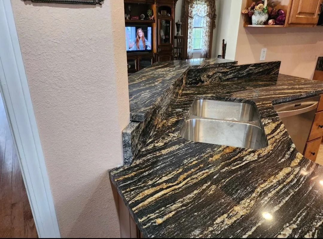 Granite countertop with sink, gold and black swirls, adjacent to wall and wooden floor in a kitchen.