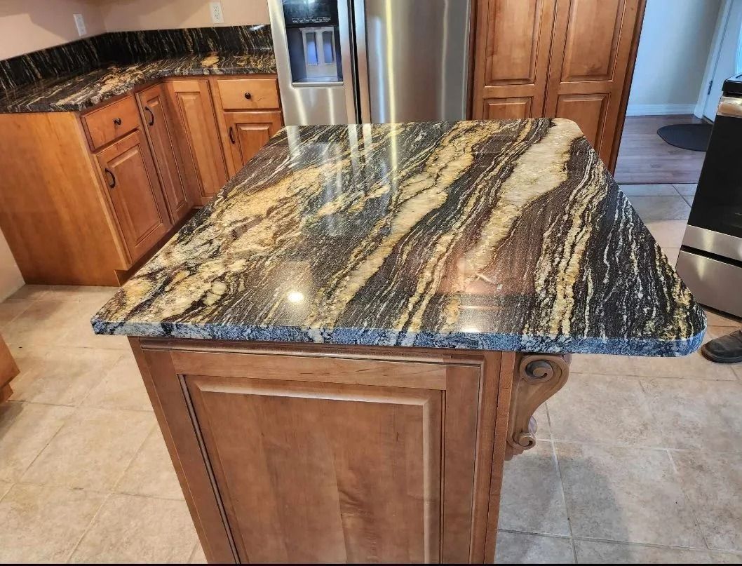 Kitchen island with brown cabinets and a granite countertop. Stainless steel fridge in the background.