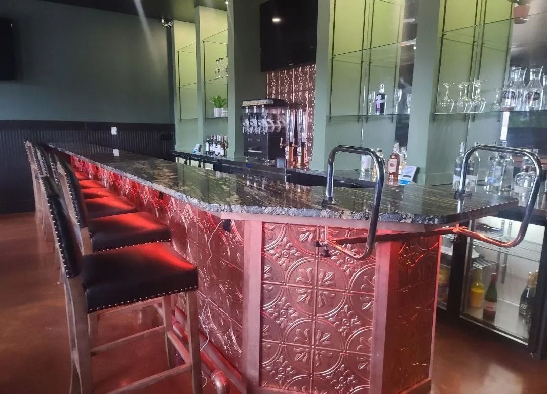 Bar interior with red and copper accents. Empty bar stools in front of a long counter.