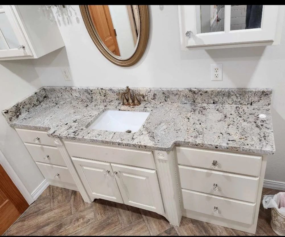 Bathroom vanity with white cabinets, granite countertop, and oval mirror.