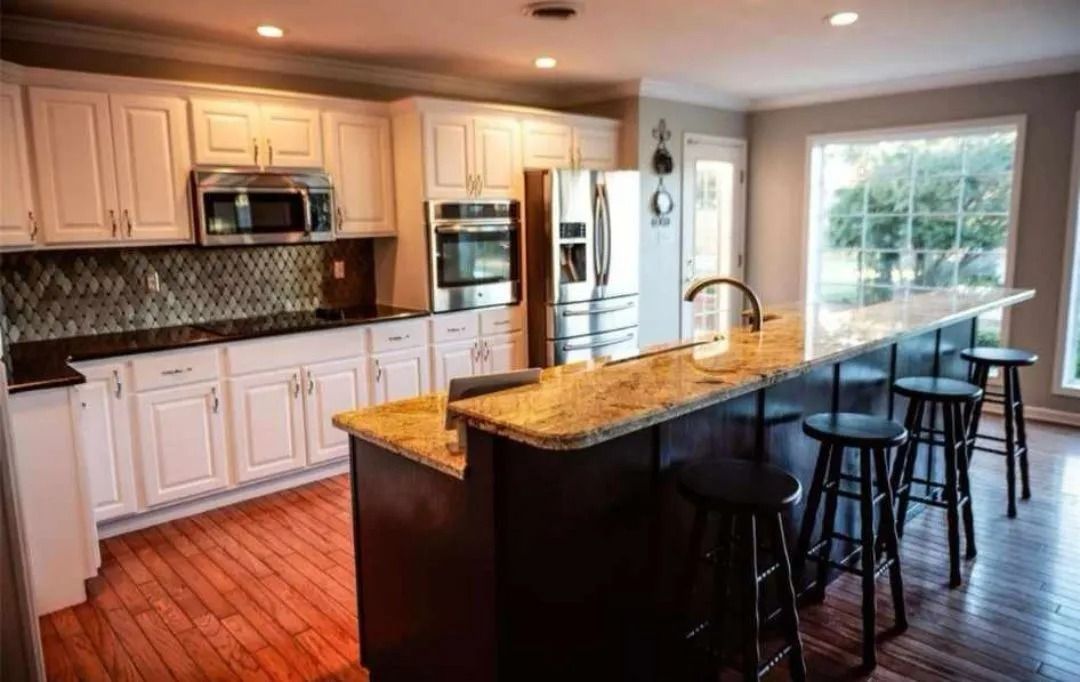 Kitchen with cream cabinets, granite countertops, and a dark wood island with bar stools.