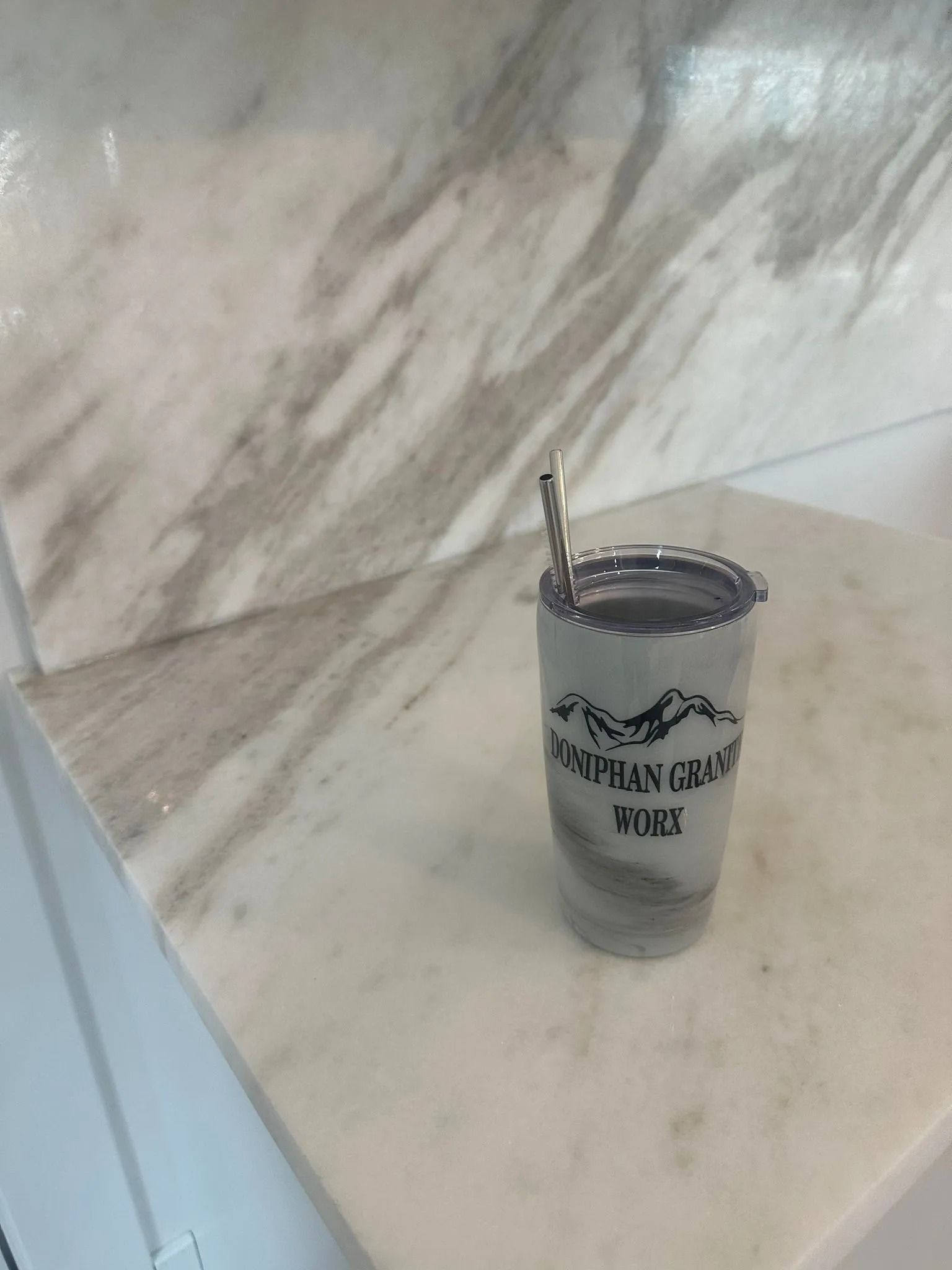 Marble-patterned tumbler with a straw, sitting on a white and gray marble surface. The tumbler says 