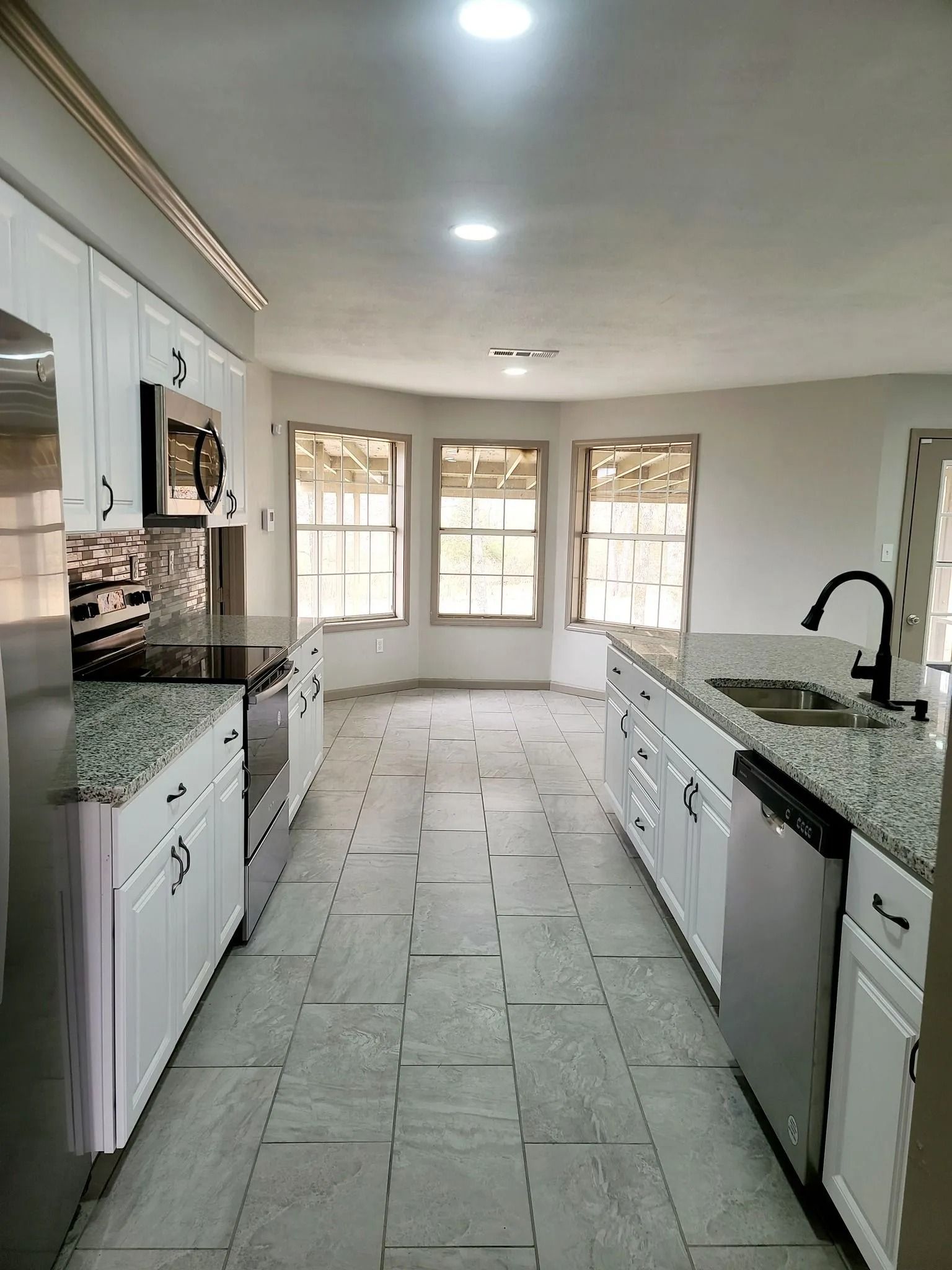 White kitchen with granite countertops, stainless steel appliances, and tile floor.